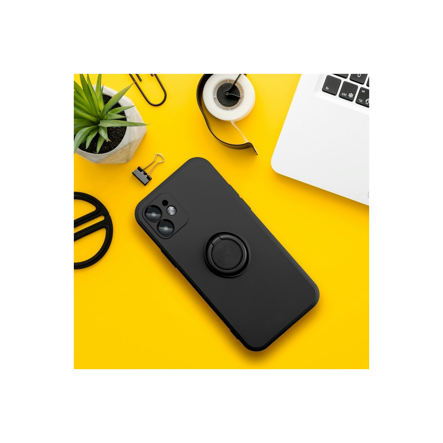Un telefono nero con un anello, con un laptop e una pianta su sfondo giallo.