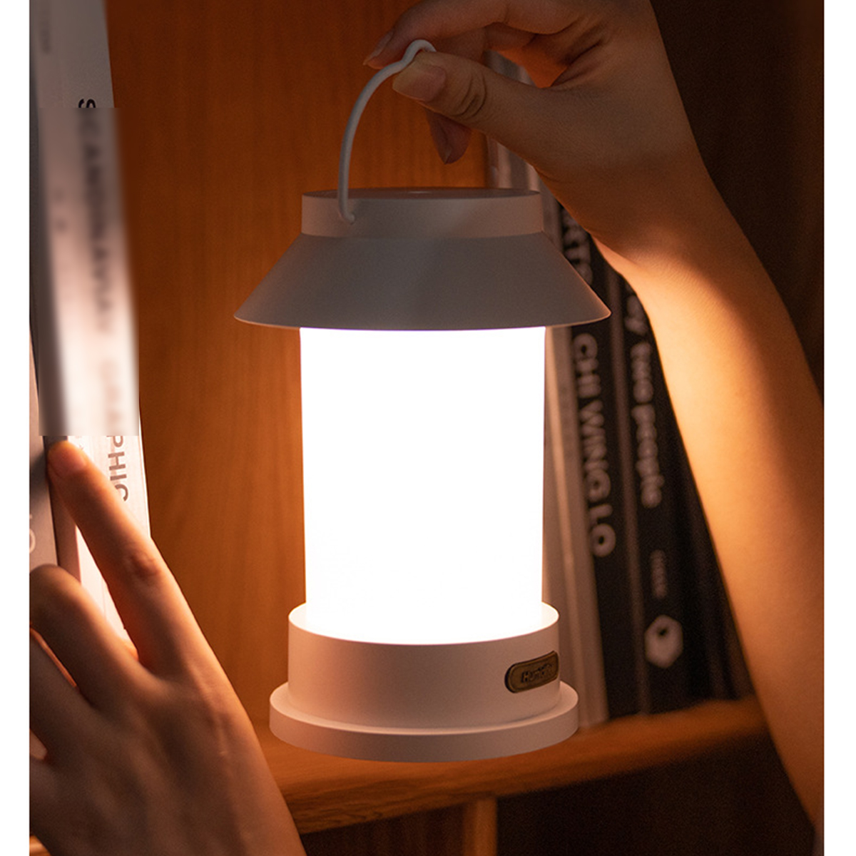 Eine weiße Laterne mit Licht, gehalten von Händen in der Nähe eines Bücherregals.