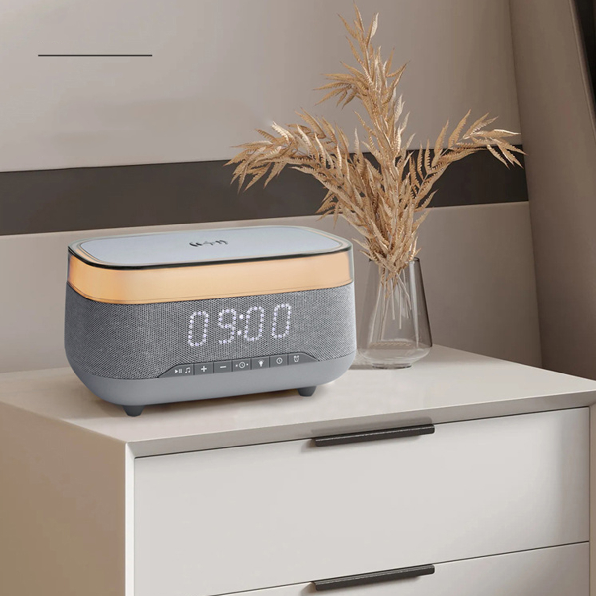 Digitaler Wecker auf einem weißen Nachttisch, mit einer dekorativen Pflanze. Die Uhr zeigt die Zeit.