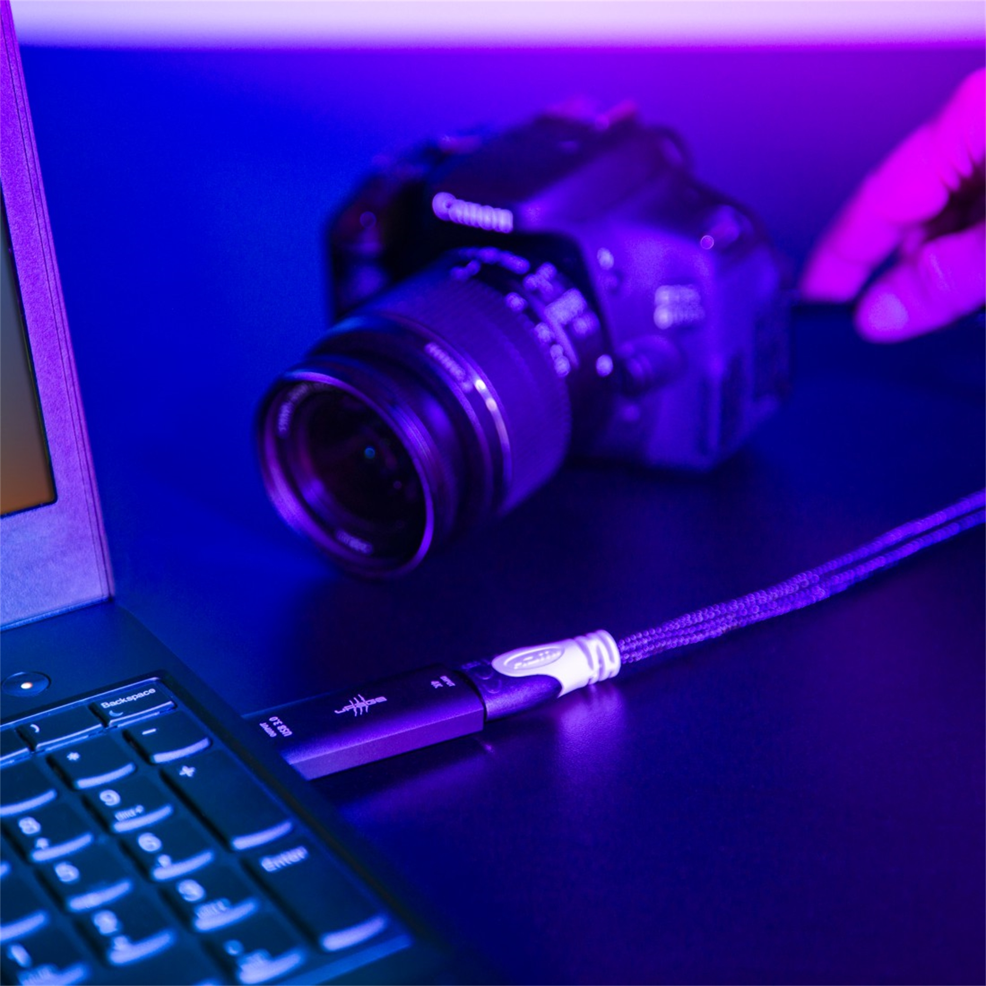 Ein Laptop mit Kabel an Kamera. Hintergrund lila/blau beleuchtet.