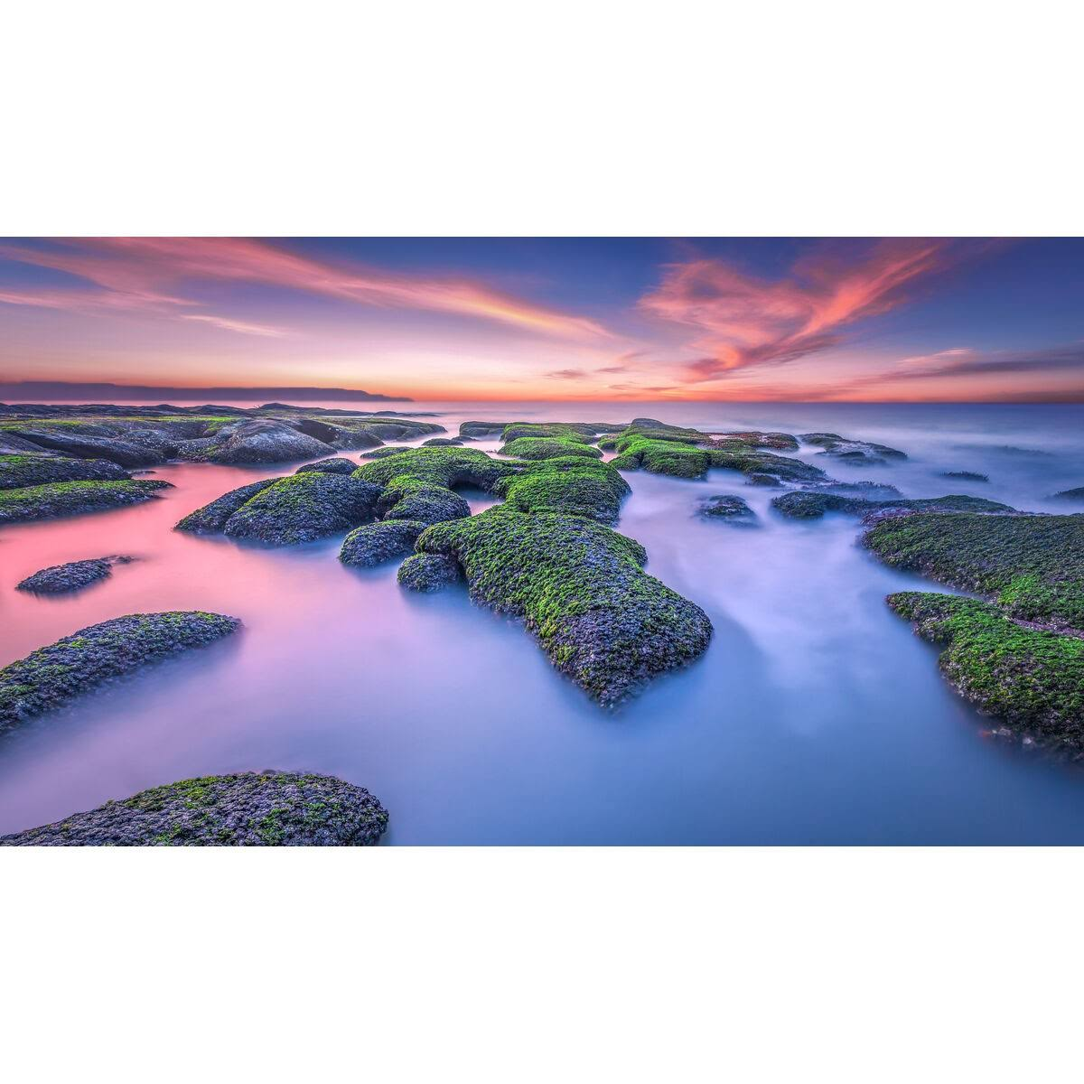 Widok na omszałe skały w wodzie z kolorowym zachodem słońca w tle.