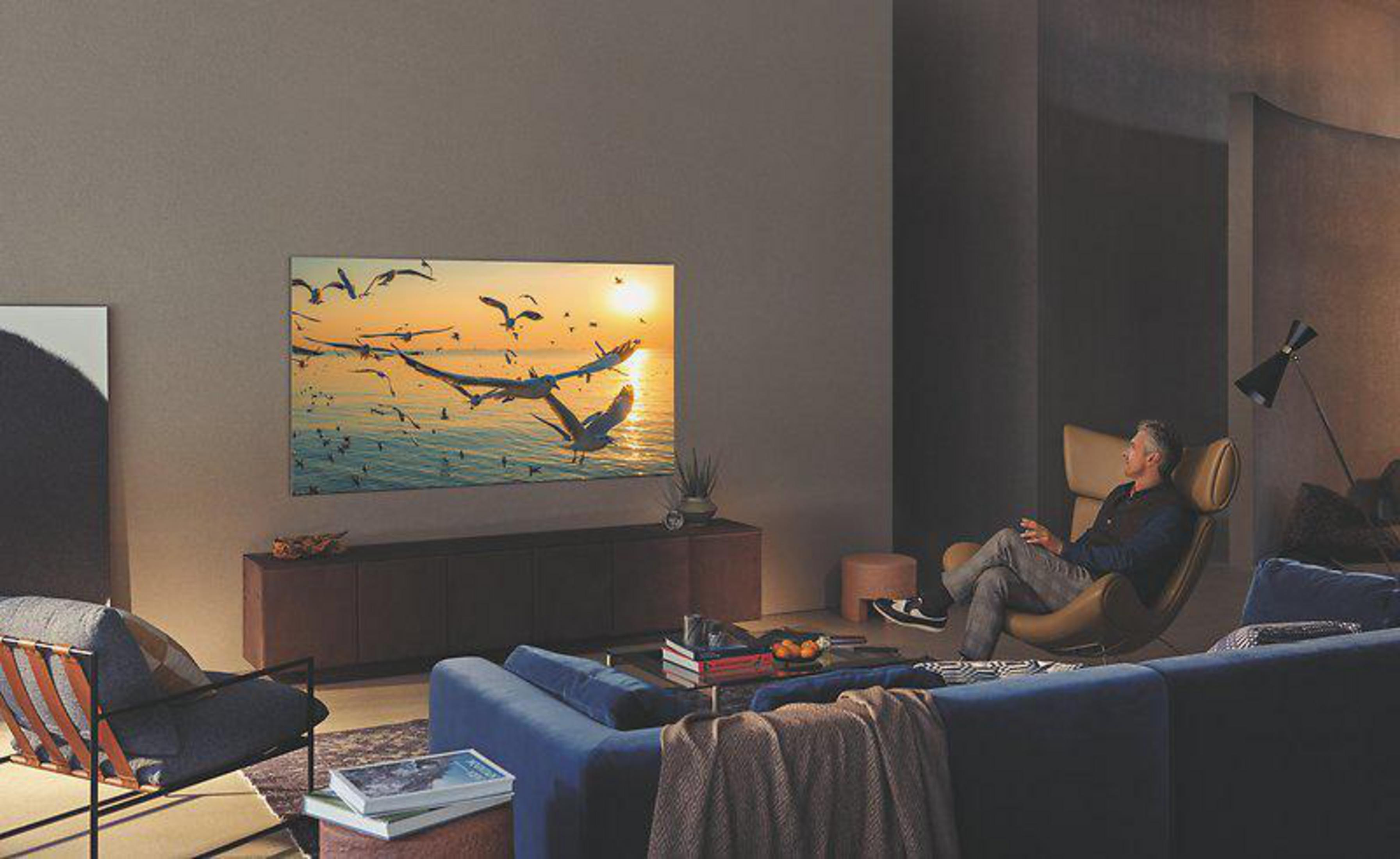 Mężczyzna siedzący na krześle ogląda duży telewizor z zachodem słońca.