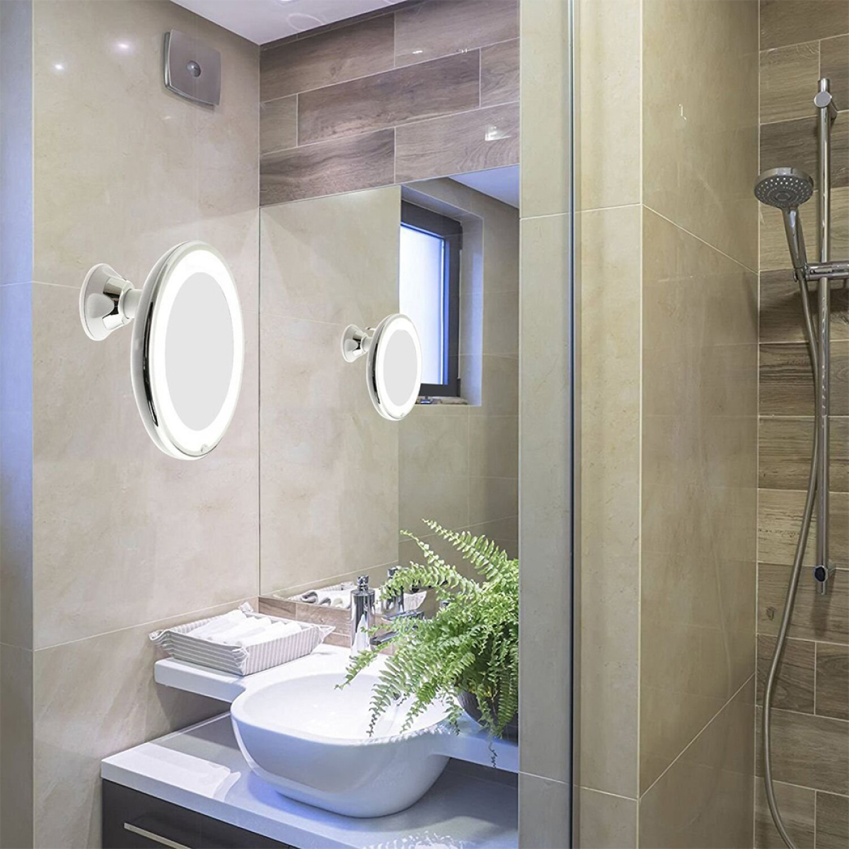 Badezimmer mit zwei beleuchteten Spiegeln, Waschbecken, Pflanze und Dusche. Beige- und Brauntöne.