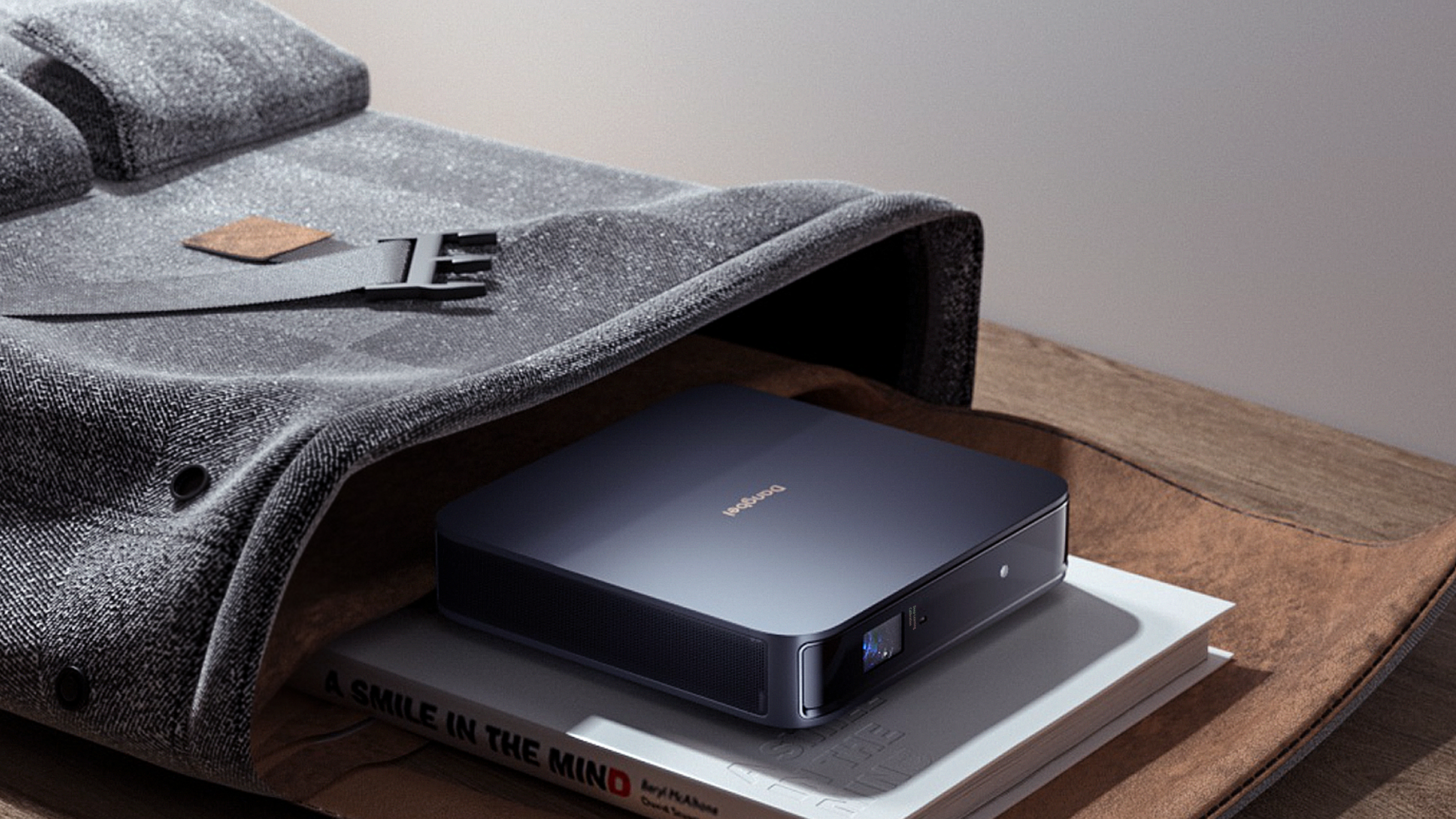 Mały, ciemnoszary projektor leżący na książce w szarej torbie.