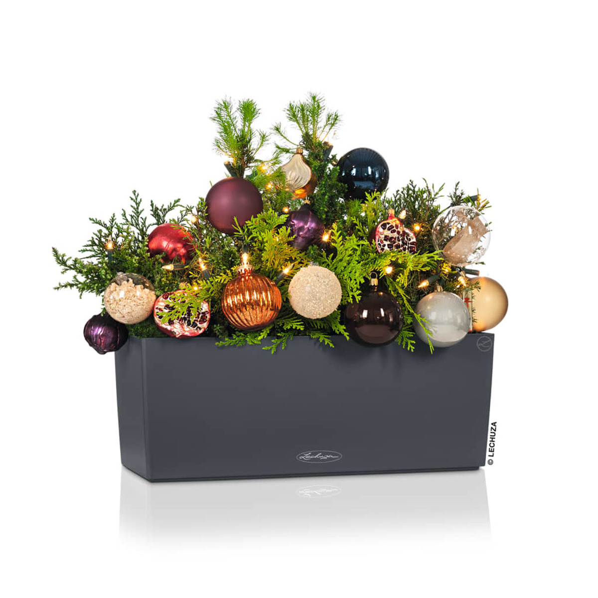 Weihnachtsarrangement in einem dunkelgrauen rechteckigen Pflanzgefäß mit Ornamenten.