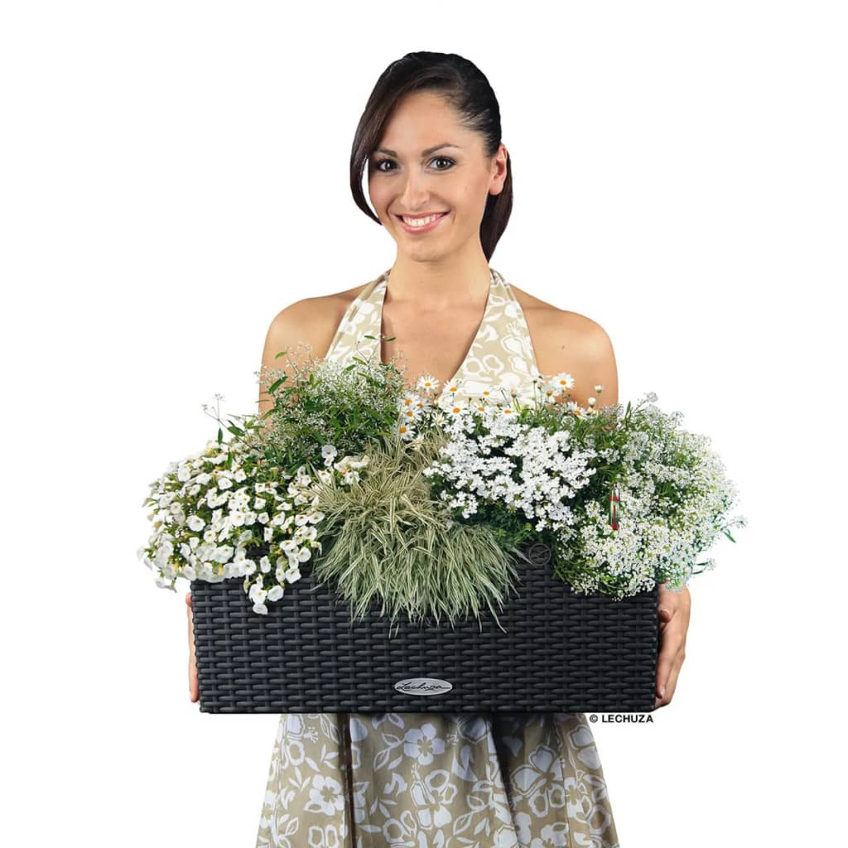 Une femme tenant une jardinière rectangulaire noire avec des fleurs, souriant, fond blanc, logo Lechuza.