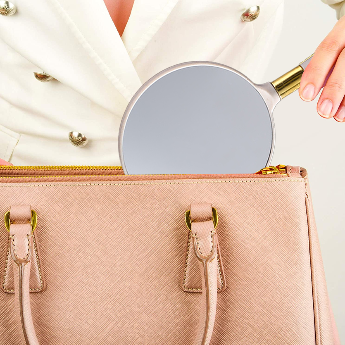 Eine Person hält einen Handspiegel über einer rosa Handtasche. Die Tasche ist halb geöffnet.
