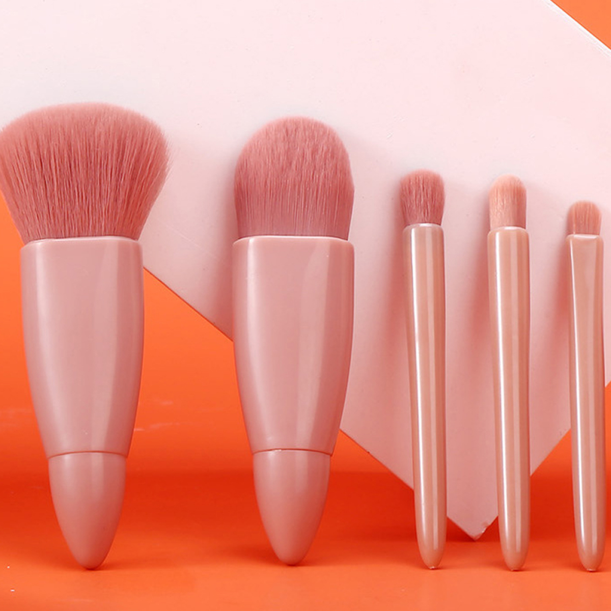 Set von rosa Make-up-Pinseln auf einer orangefarbenen Oberfläche.