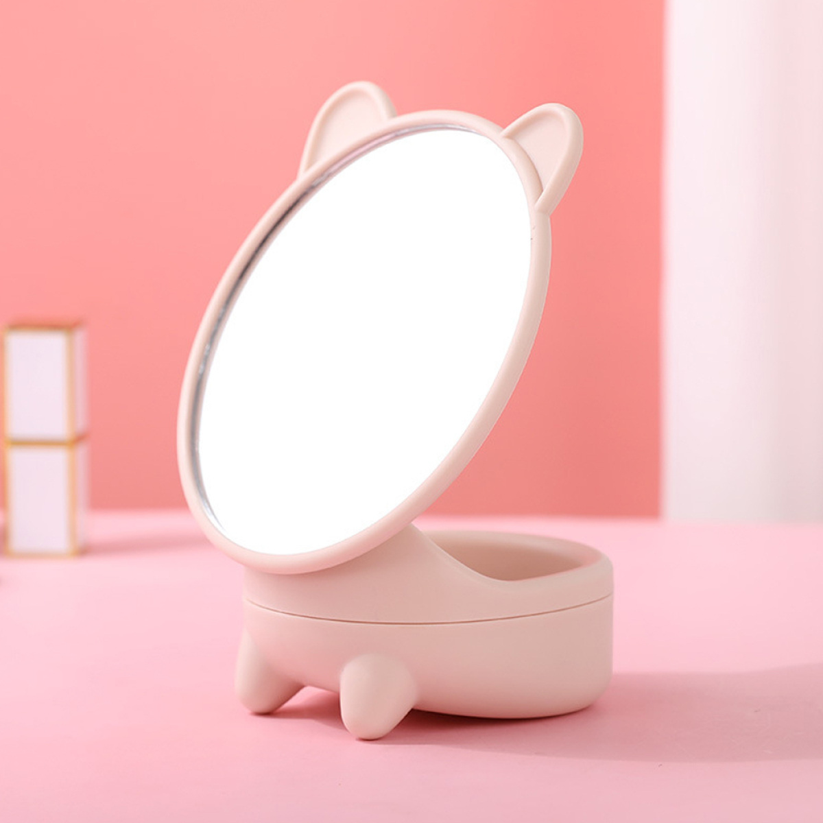 Ein rosa katzenförmiger Spiegel auf rosa Oberfläche, mit kleinem Staufach.