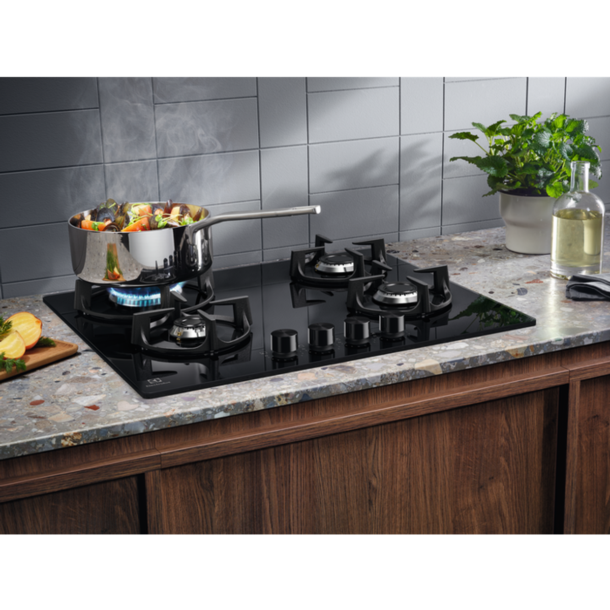 Czarna płyta grzejna z garnkiem, jedzeniem i płomieniami. Otoczenie kuchni z drewnianymi szafkami i kamiennym blatem.