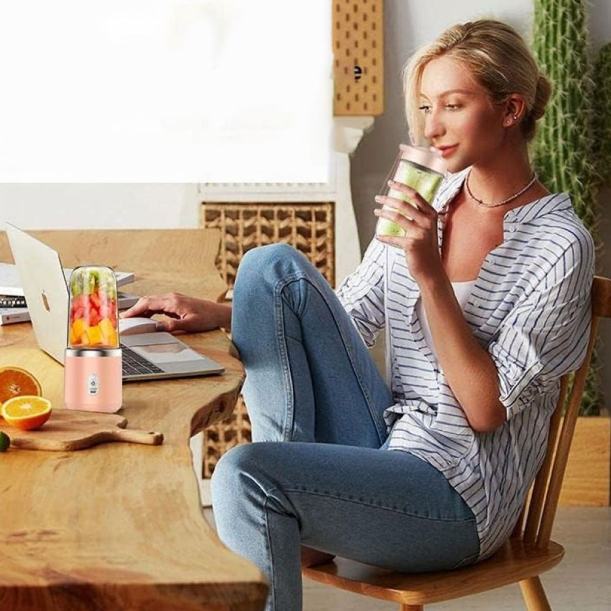 Frau arbeitet am Laptop mit Mixer und Obst daneben.