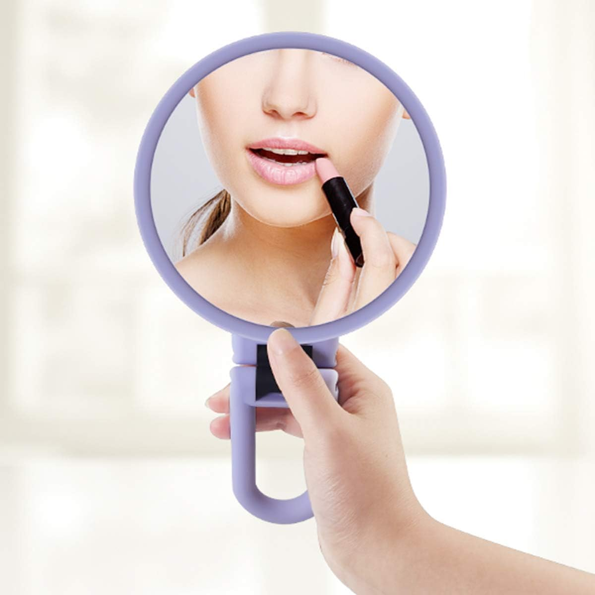 Frau trägt Lippenstift in einem lila Handspiegel auf. Verschwommener Hintergrund.