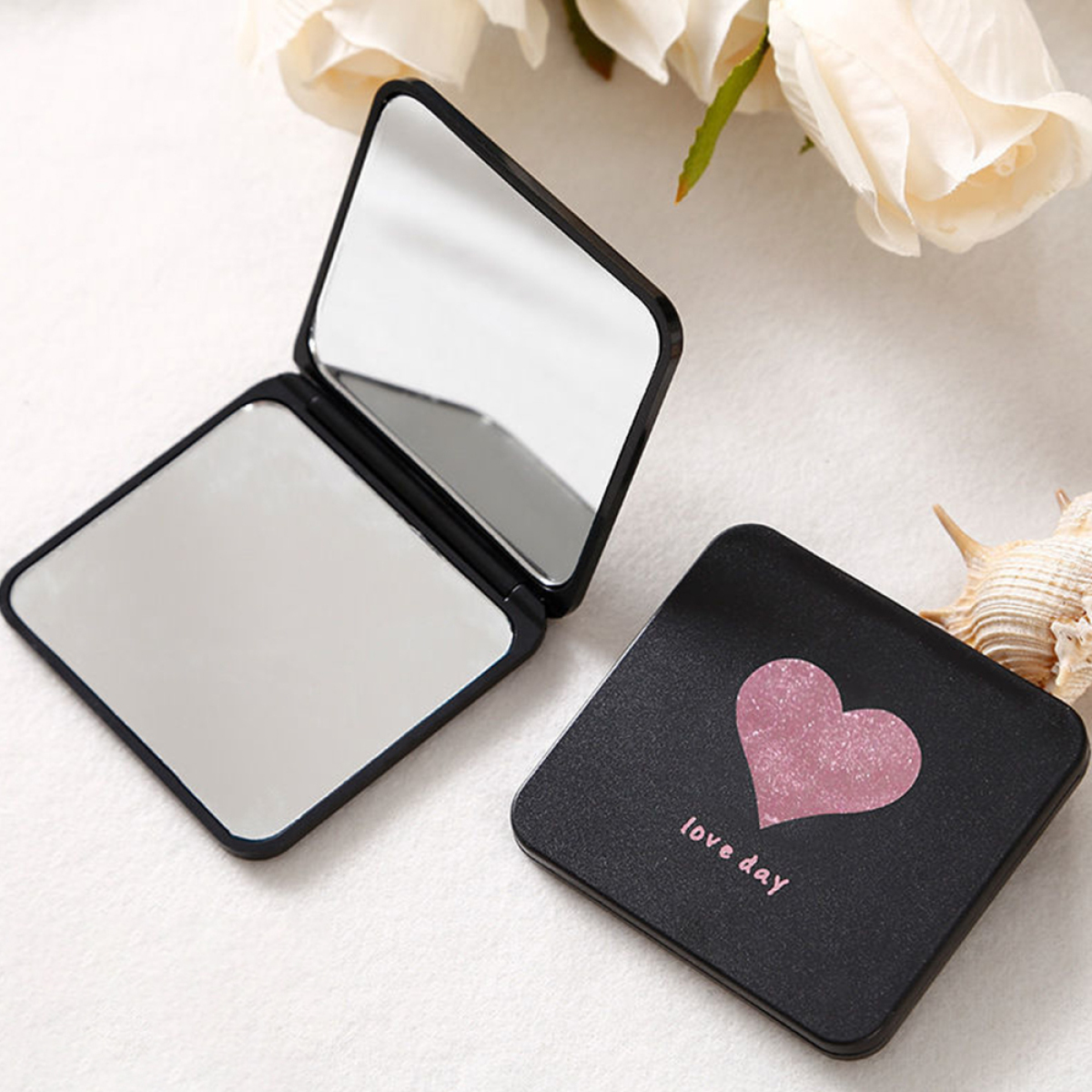 Schwarzer Klappspiegel. Eine Seite offen, andere geschlossen. Rosa Herz und "love day" auf dem Deckel.
