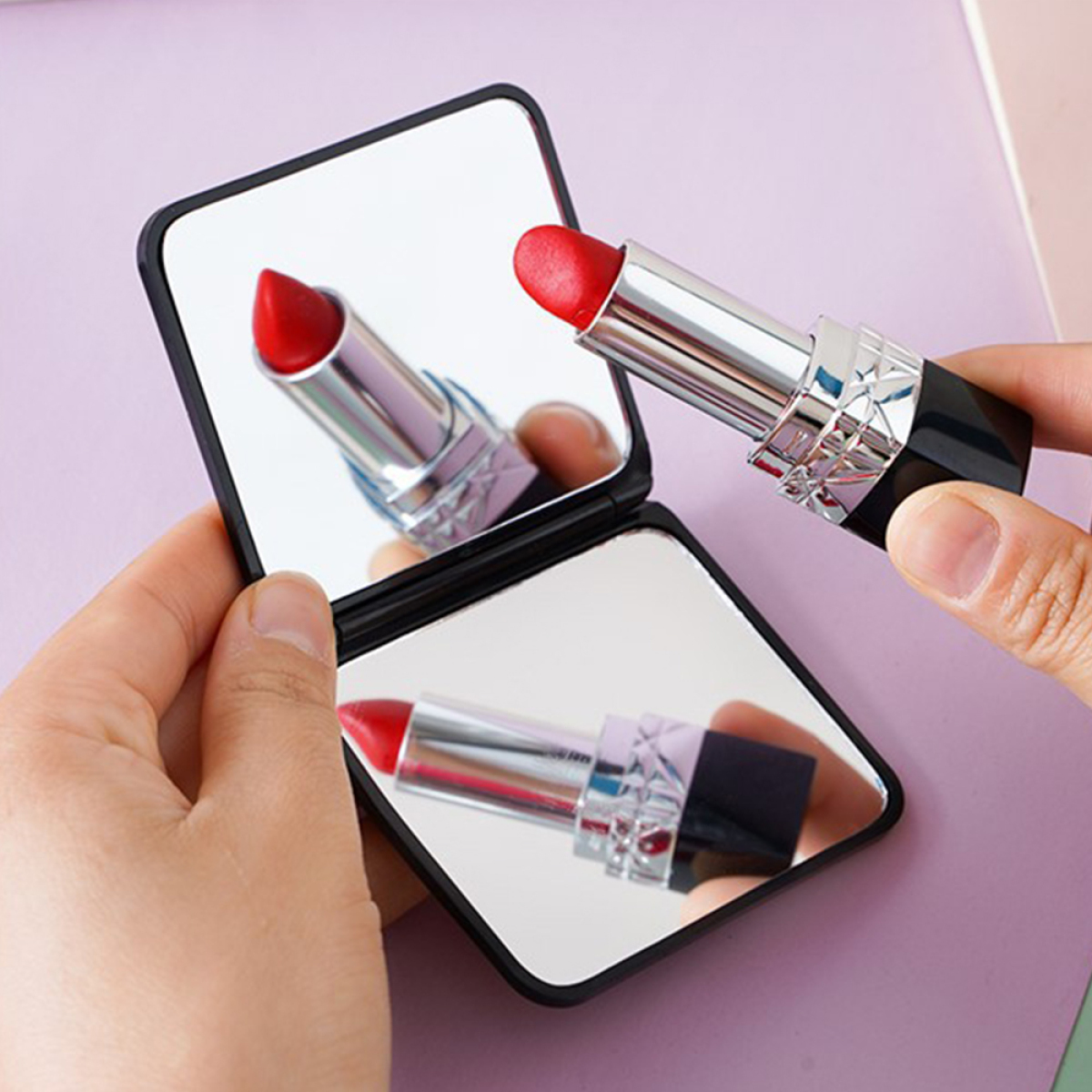 Eine Person hält einen offenen, verspiegelten Kompaktspiegel mit rotem Lippenstift; zeigt die Reflexion des Lippenstifts.
