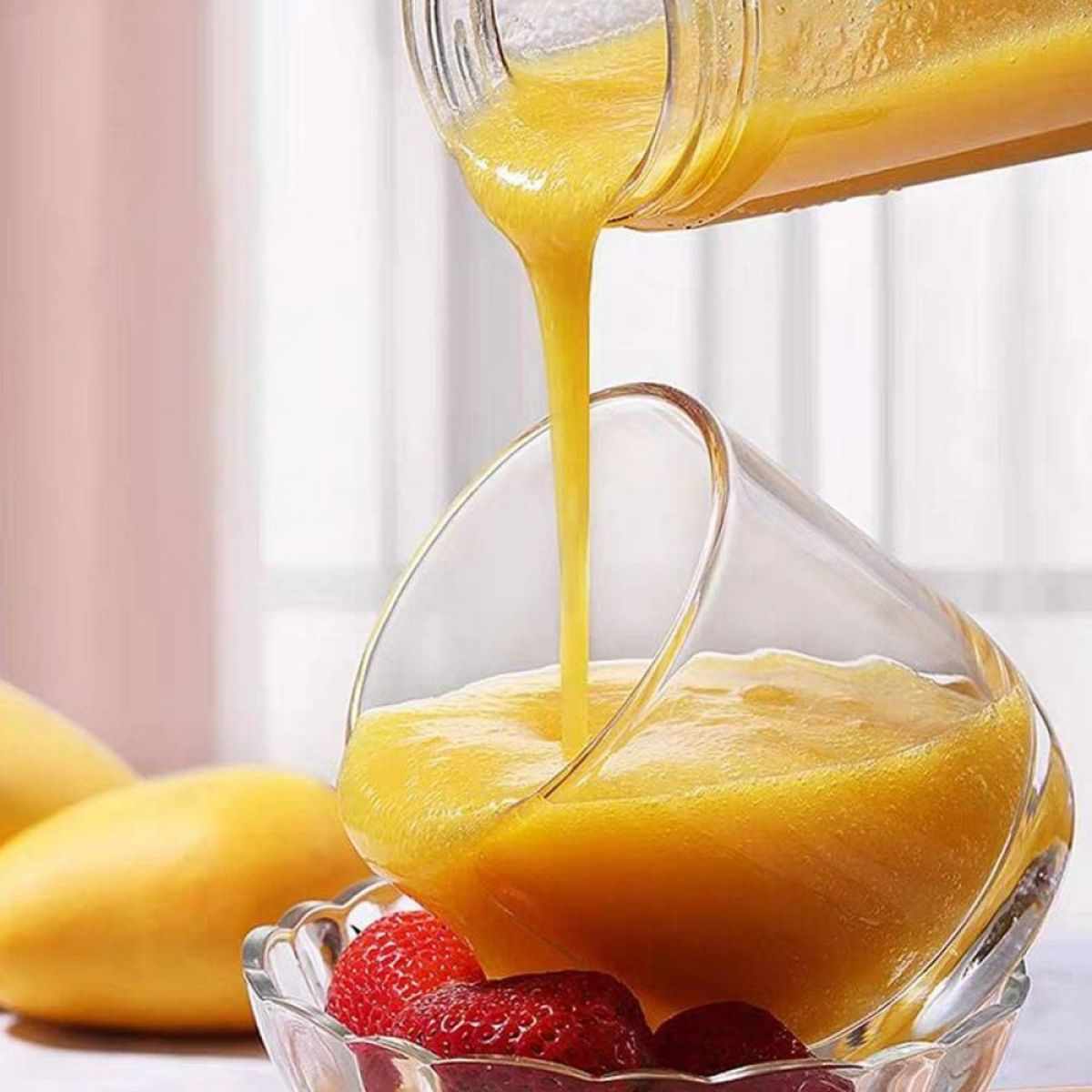 Mangosaft gießt in ein Glas mit Erdbeeren. Mangos sind an der Seite.