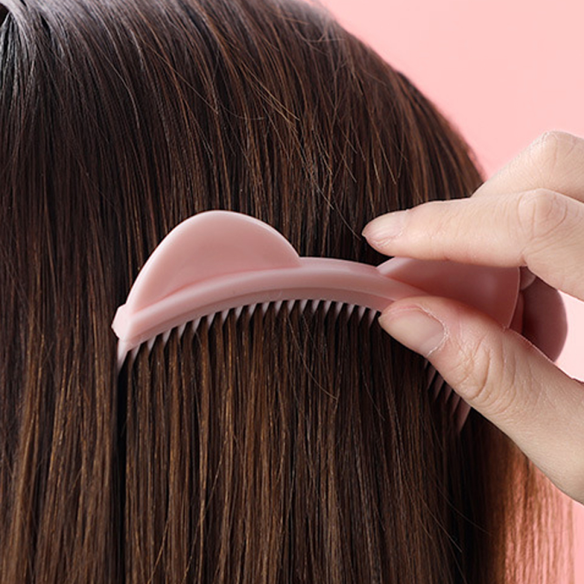 Eine Hand, die braunes Haar mit einem rosa Kamm kämmt, Nahaufnahme des Vorgangs.