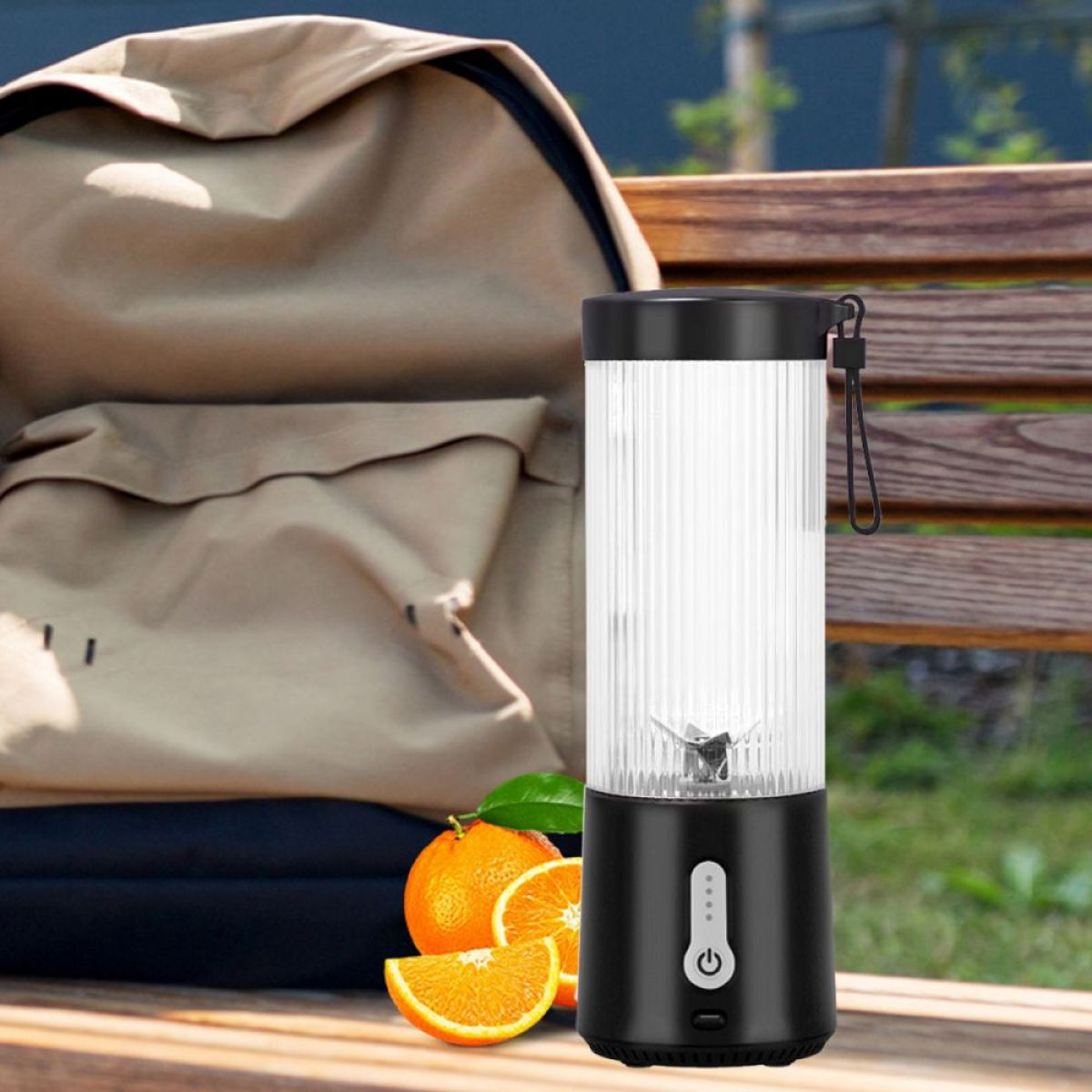 Schwarz-weißer Mixer mit Orangenscheiben und Orangen. Hintergrund: Rucksack, Bank und Gras.