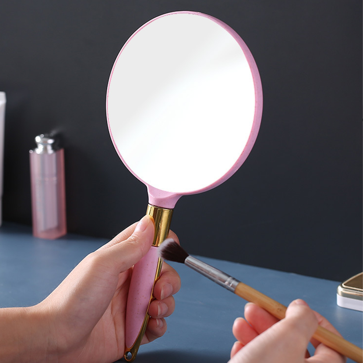 Ein rosa Handspiegel mit goldenem Griff wird für Make-up verwendet.