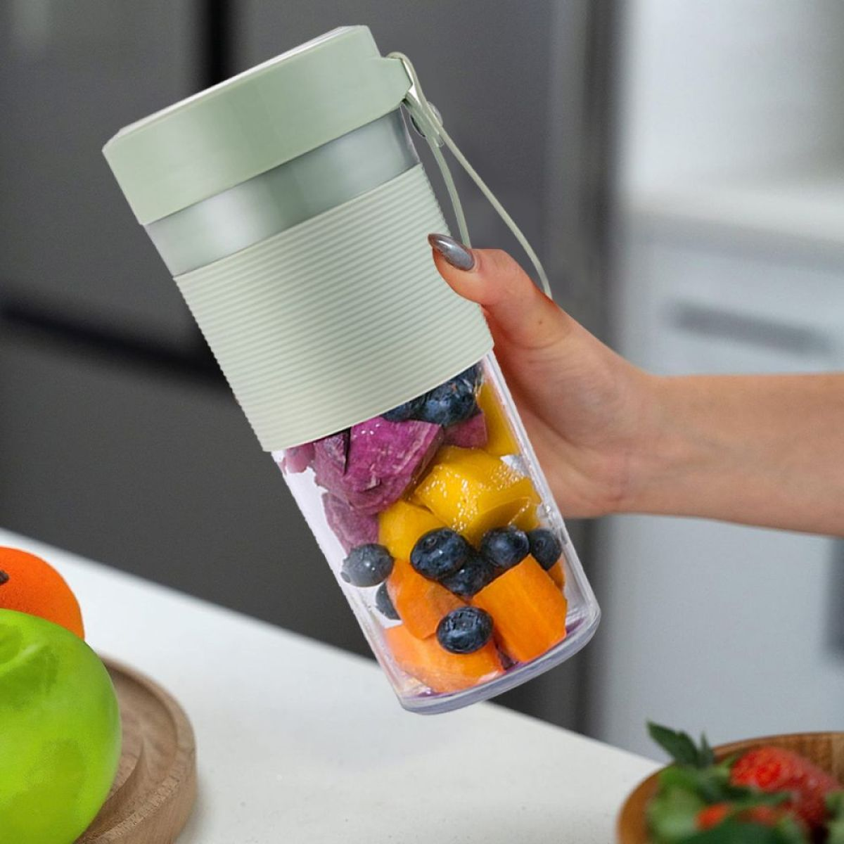 Eine Hand hält einen Mixer mit geschnittenen Früchten im Inneren.