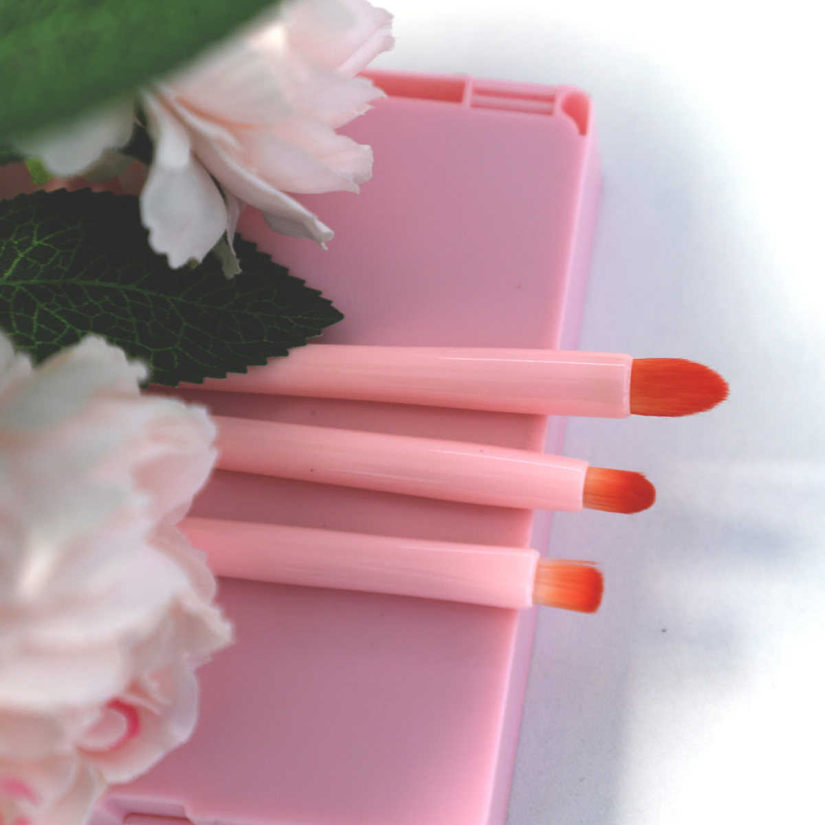 Pinke Make-up-Pinsel liegen auf einer pinken Make-up-Palette, mit floralen Akzenten.