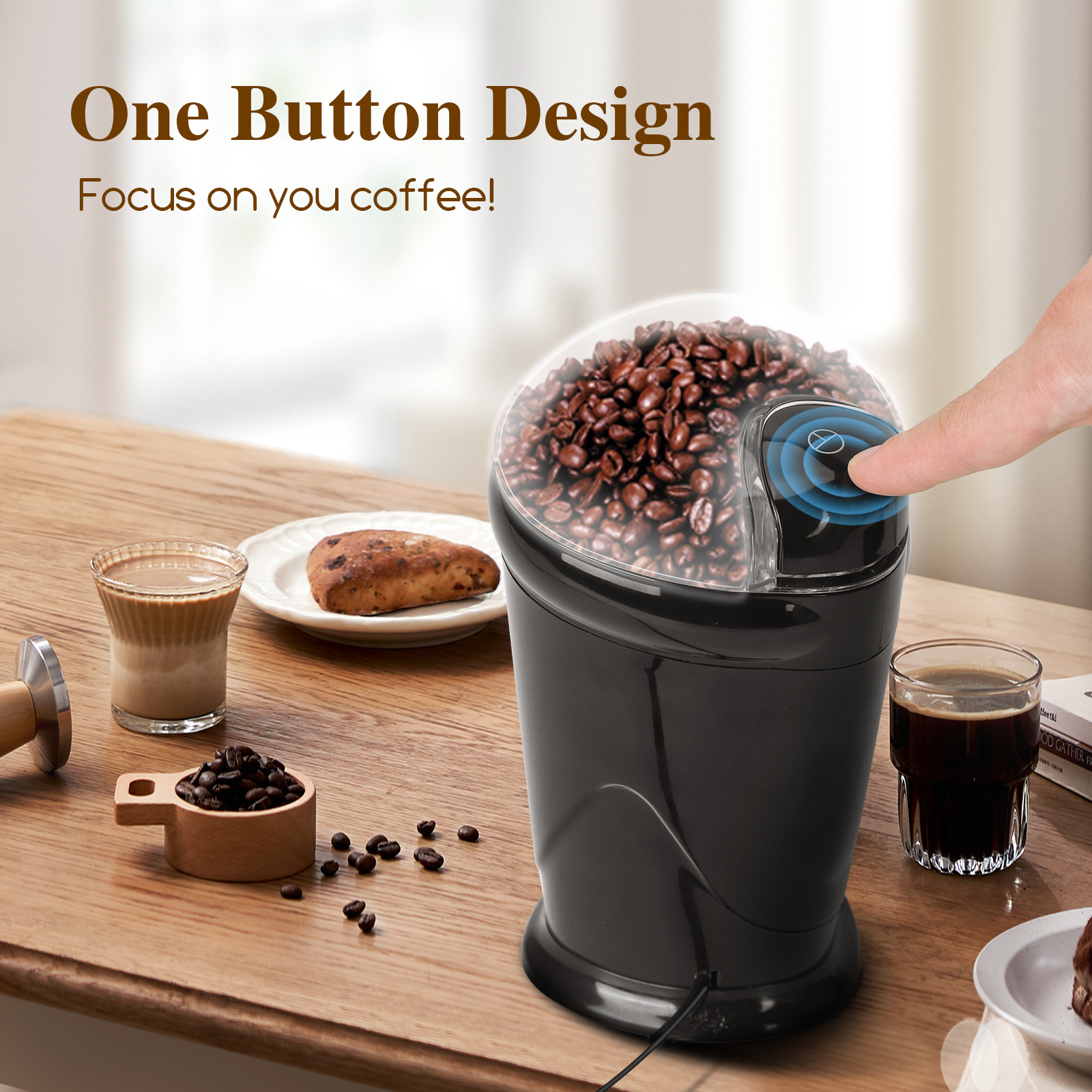 Molinillo de café con granos, un dedo presionando un botón. Otros elementos de café en la mesa.