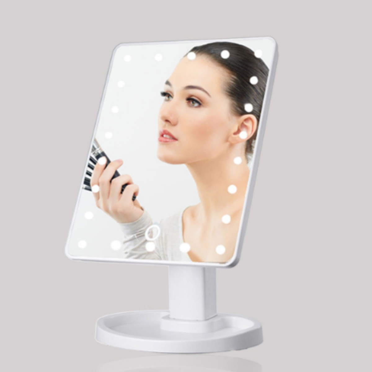 Frau blickt in einen beleuchteten Schminkspiegel, hält einen Make-up-Pinsel, mit neutralem Hintergrund.