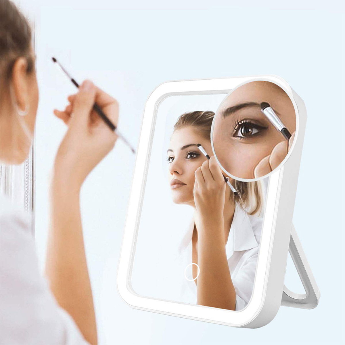 Eine Frau schaut in einen Spiegel mit Licht drumherum und trägt Make-up auf.