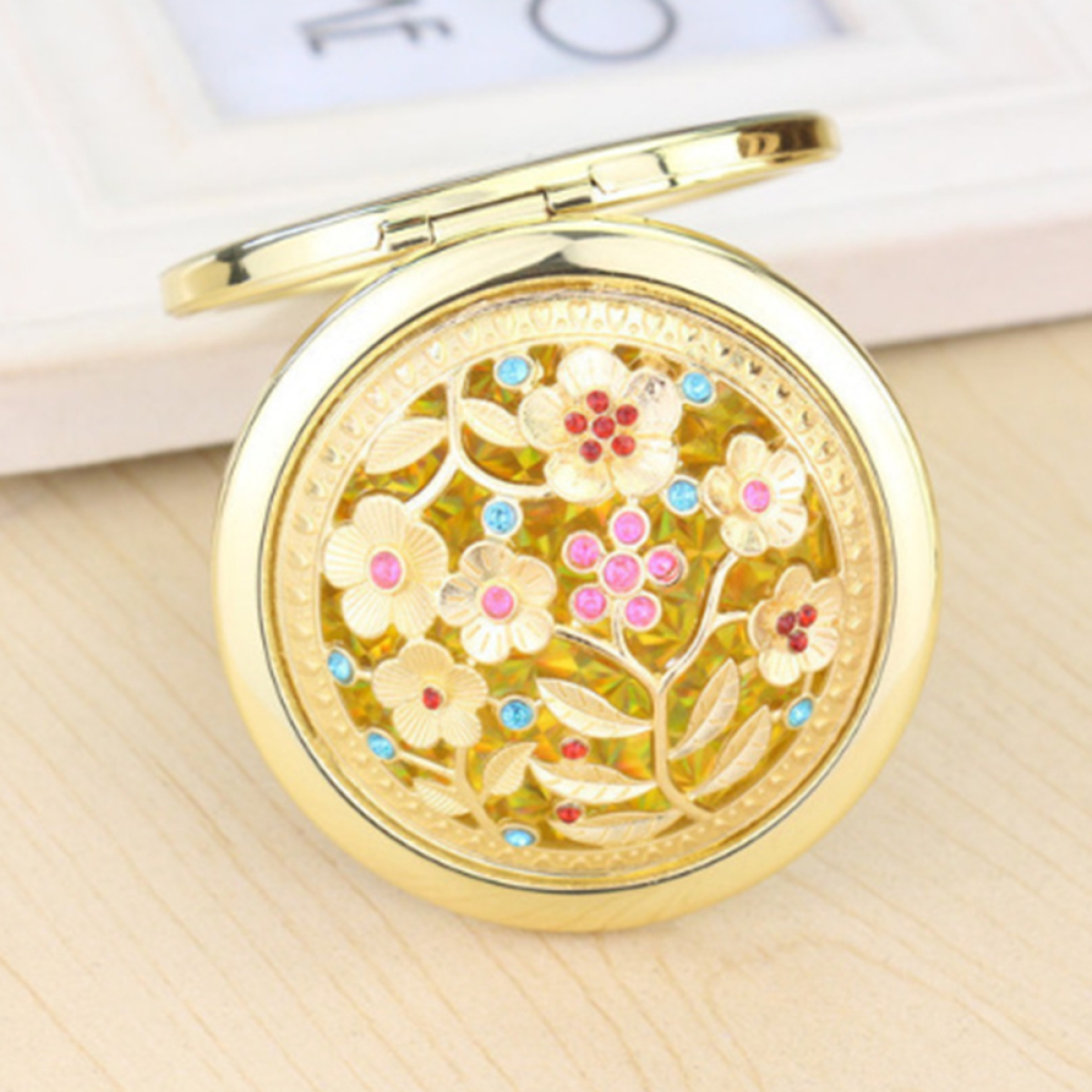 Runder, goldener Kompaktspiegel mit Blumendesign. Der Spiegel ist geöffnet.