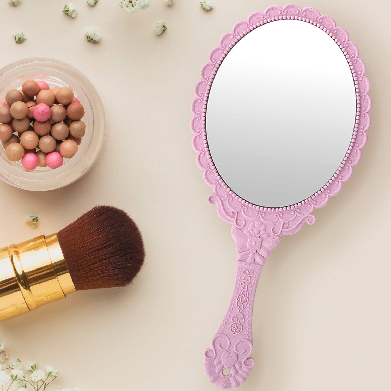 Handspiegel, Make-up-Pinsel und Tiegel mit Make-up-Kugeln auf heller Oberfläche.
