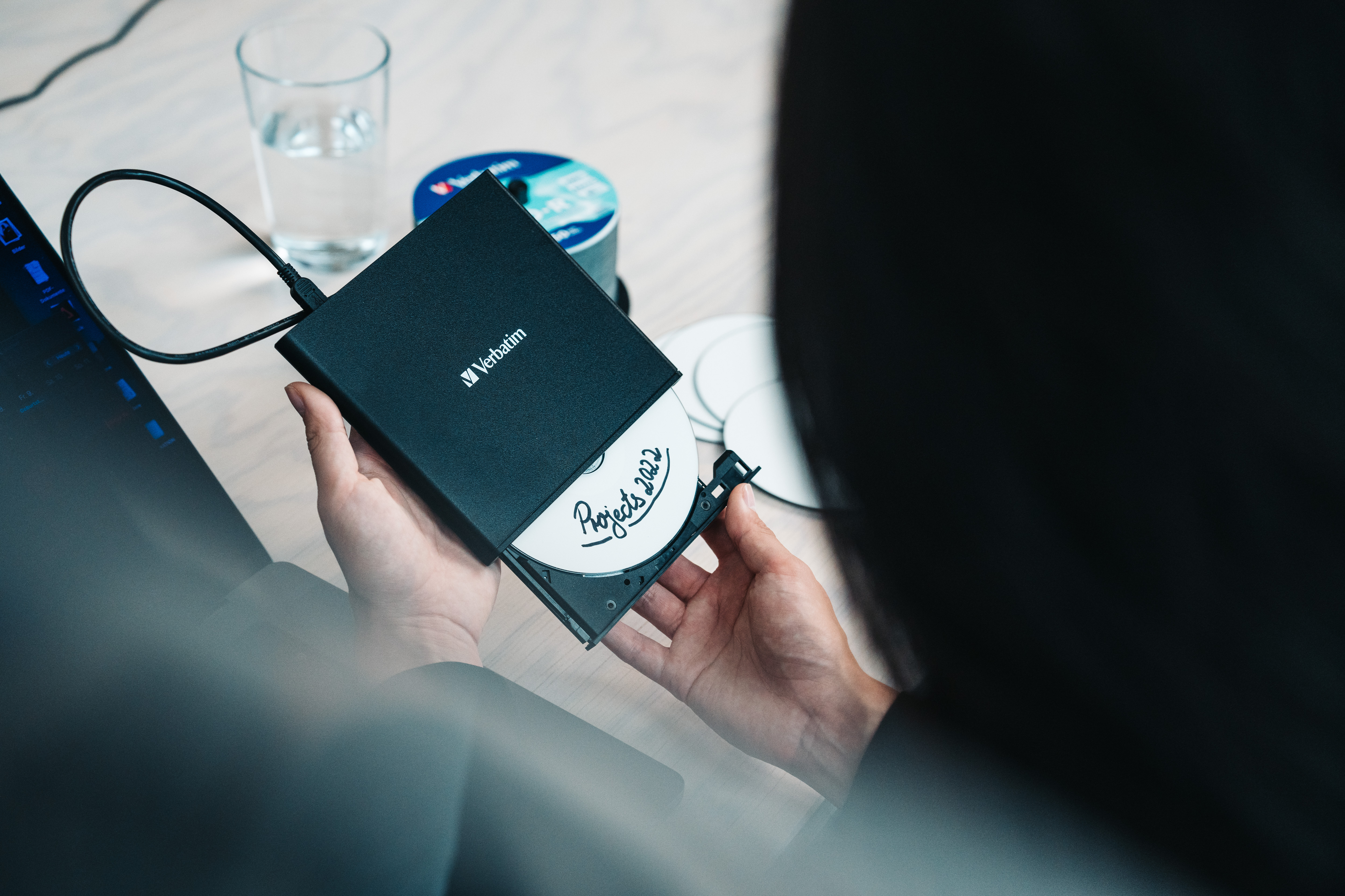 Person holding a black Verbatim external CD/DVD writer with a disc labeled 'Projects 2022'.