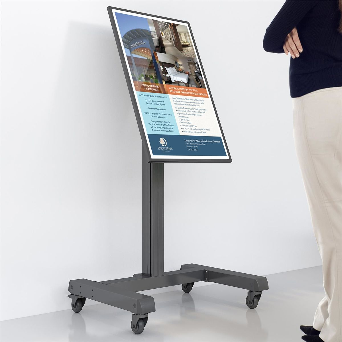 A display stand with a screen showing an advertisement. A person stands beside the stand.