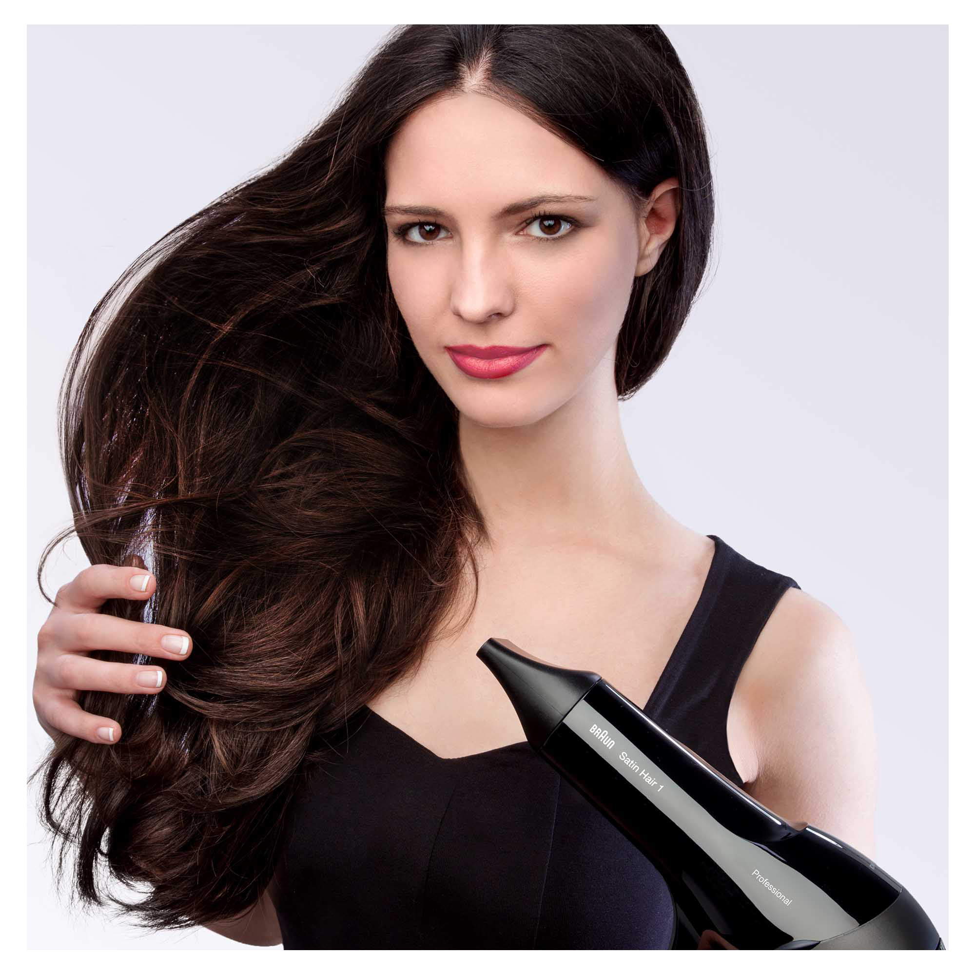 Kobieta używa czarnej suszarki, trzymając włosy. Ciemne włosy. Czarny top. Białe tło.