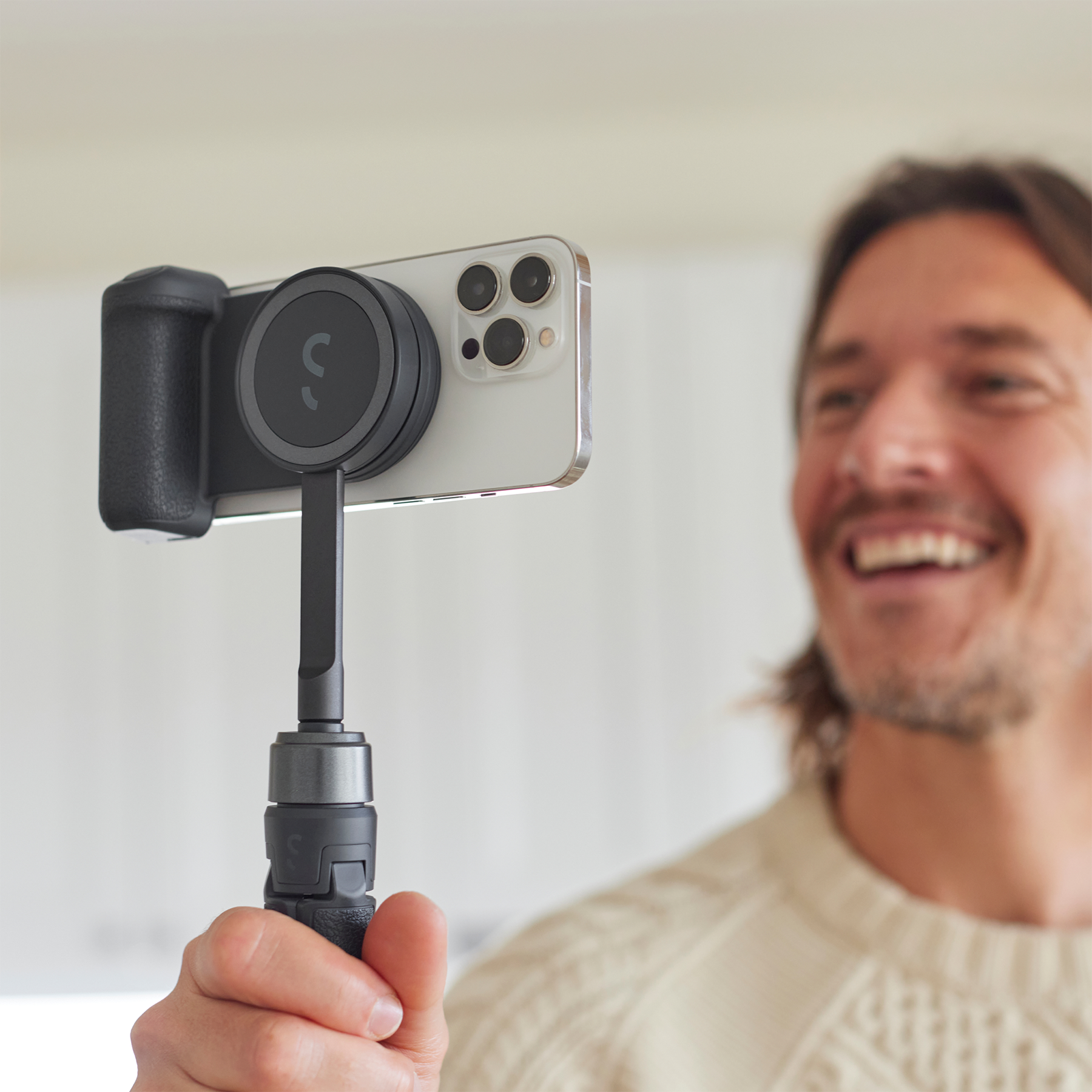 Ein lächelnder Mann hält ein Telefon, das an einem Stabilisator befestigt ist. Das Telefon zeigt zur Kamera.