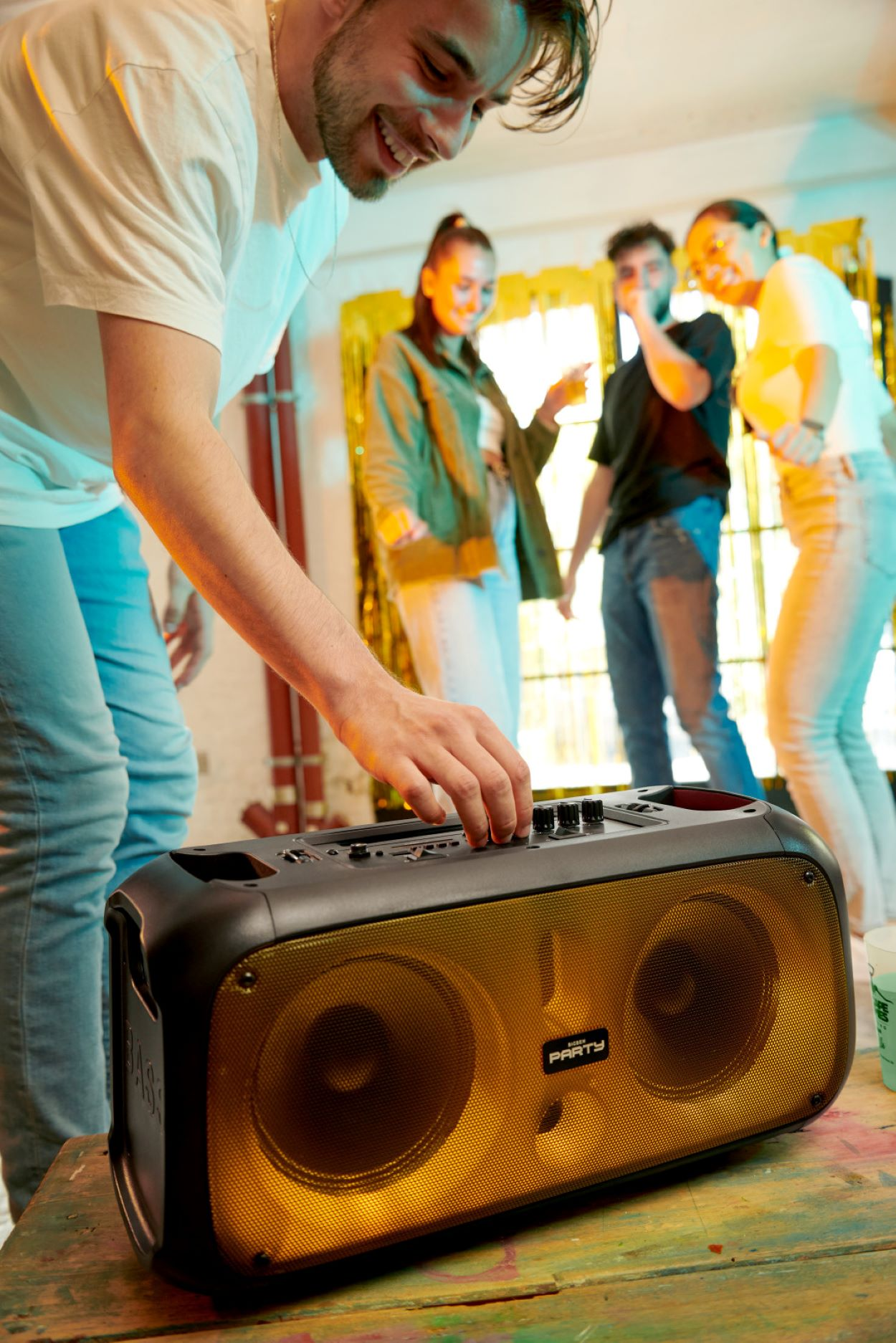 Grupa ludzi na imprezie, z mężczyzną regulującym pokrętła dużego, podświetlanego głośnika.