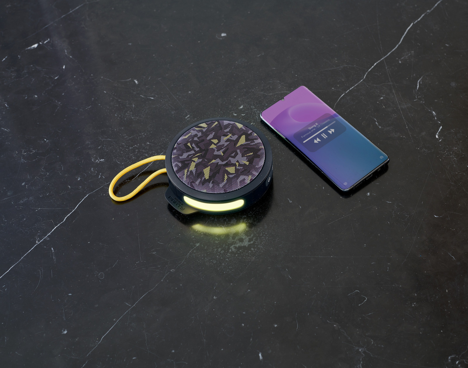 Un altoparlante portatile e un telefono su una superficie di marmo. Lo schermo del telefono mostra un'app musicale.