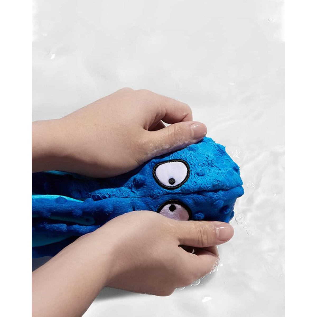 Hände, die ein blaues Oktopus-Spielzeug im Wasser waschen. Das Spielzeug hat weiße Augen und ist aus Stoff.