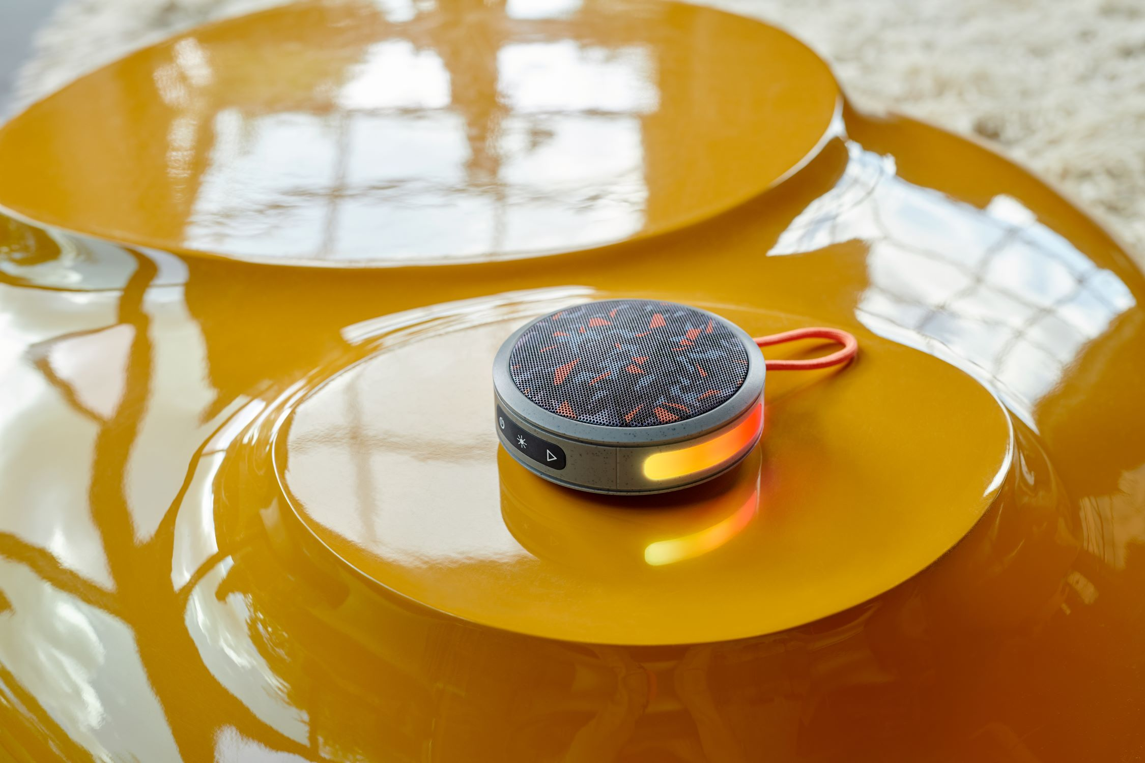 Tavolo giallo con un piccolo altoparlante rotondo grigio con accenti arancioni.