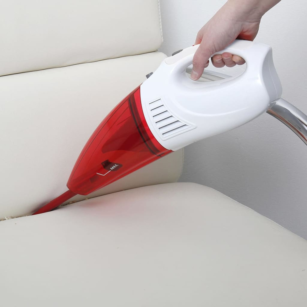 Hand verwendet einen rot-weißen Handstaubsauger auf einem weißen Sofa.