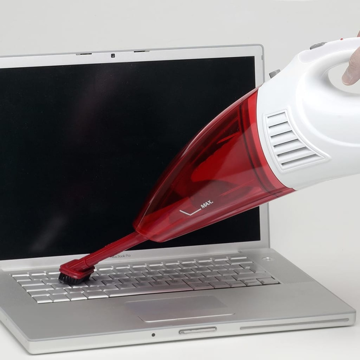 Ein roter und weißer Handstaubsauger reinigt eine Laptop-Tastatur.