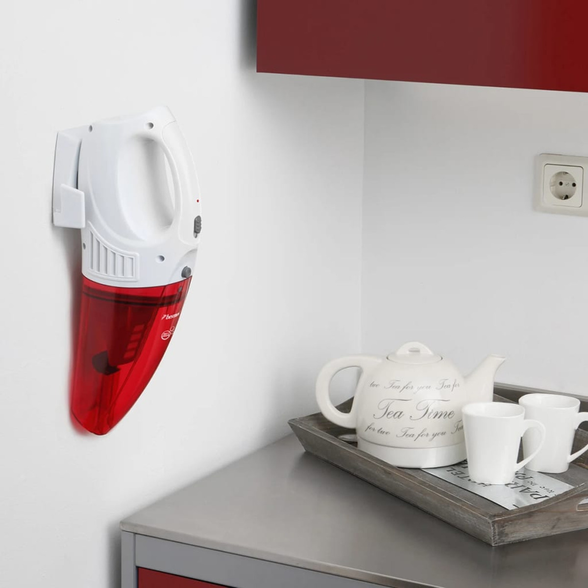 Ein weiß-roter Handstaubsauger an der Wand, mit einem Teekannenset auf einer Theke.