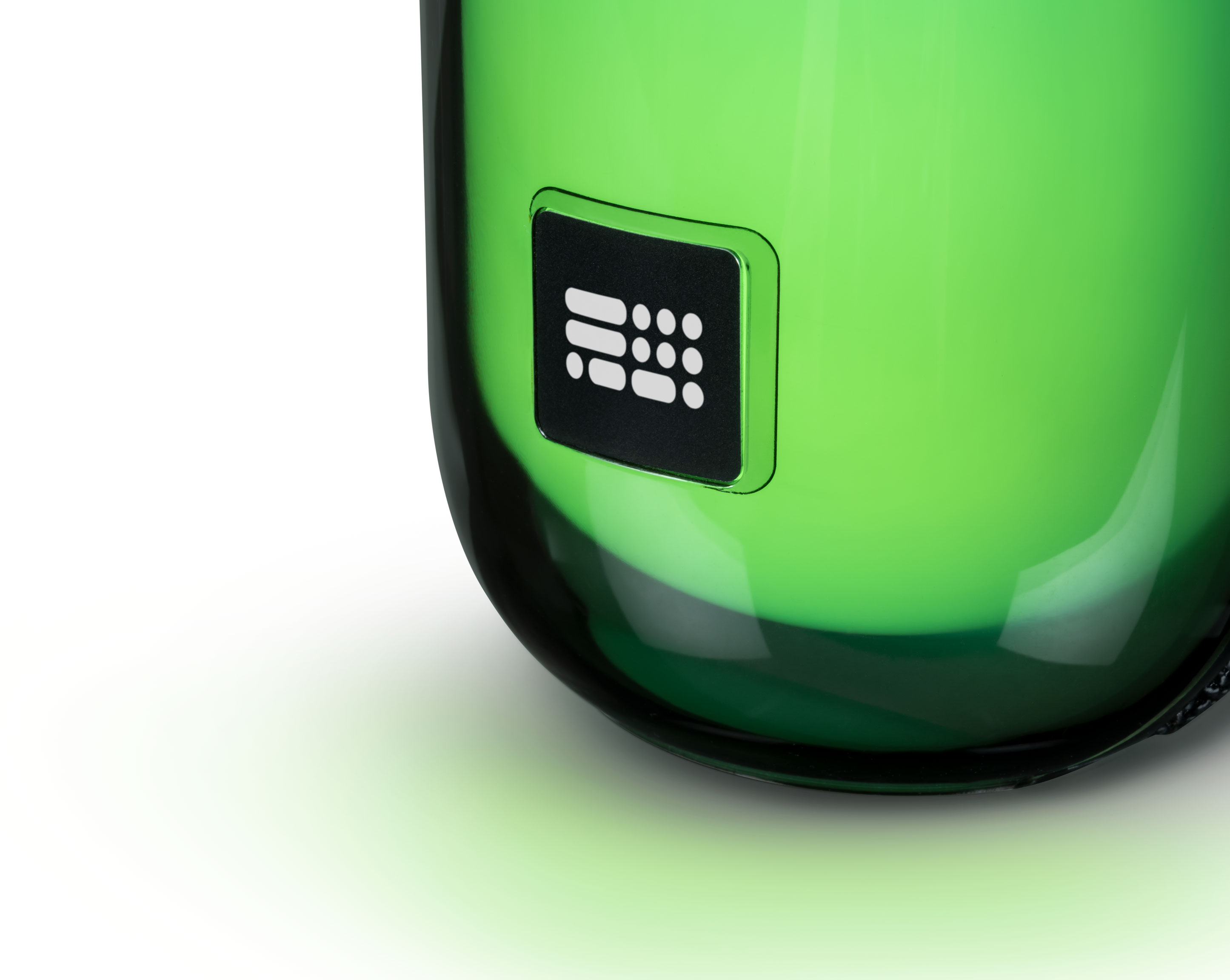 Zielony szklany przedmiot z małym czarnym kwadratem z białymi kropkami na białej powierzchni.