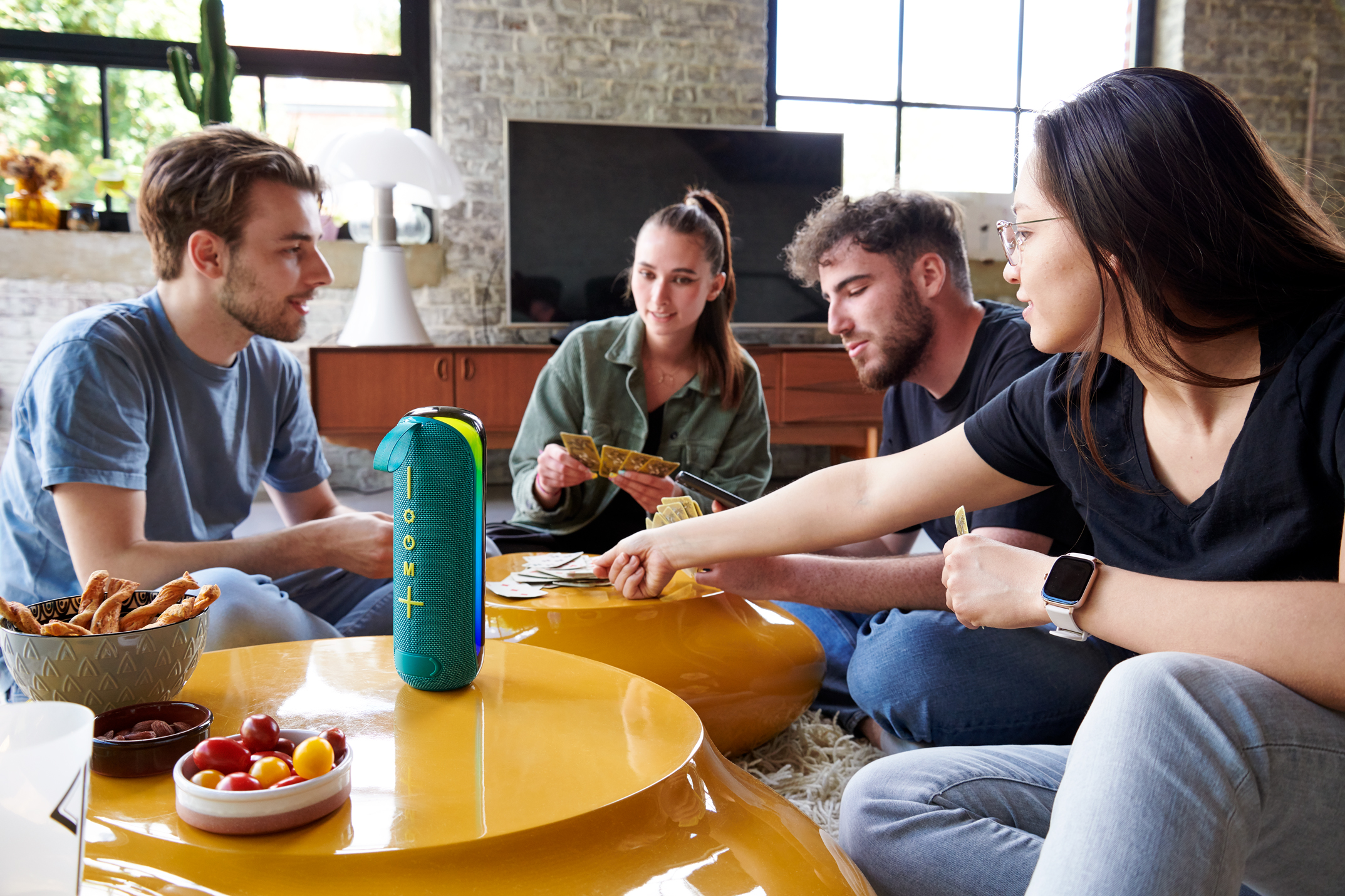 Grupa przyjaciół grających w karty z głośnikiem. Widoczne przekąski.