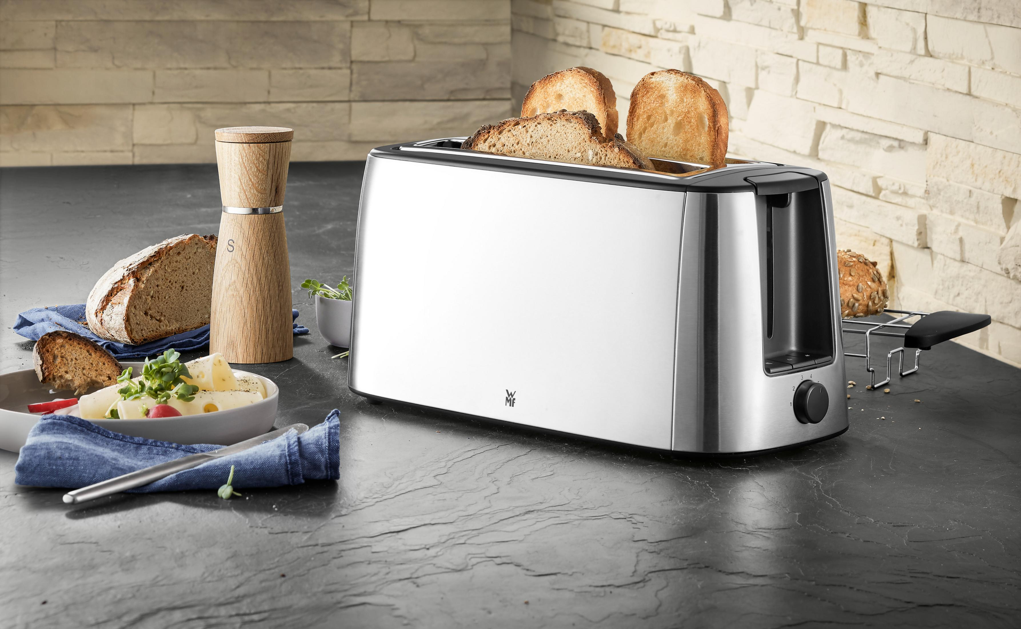 Silberner Toaster mit herausspringendem Toast, Brot, Butter und Zutaten.