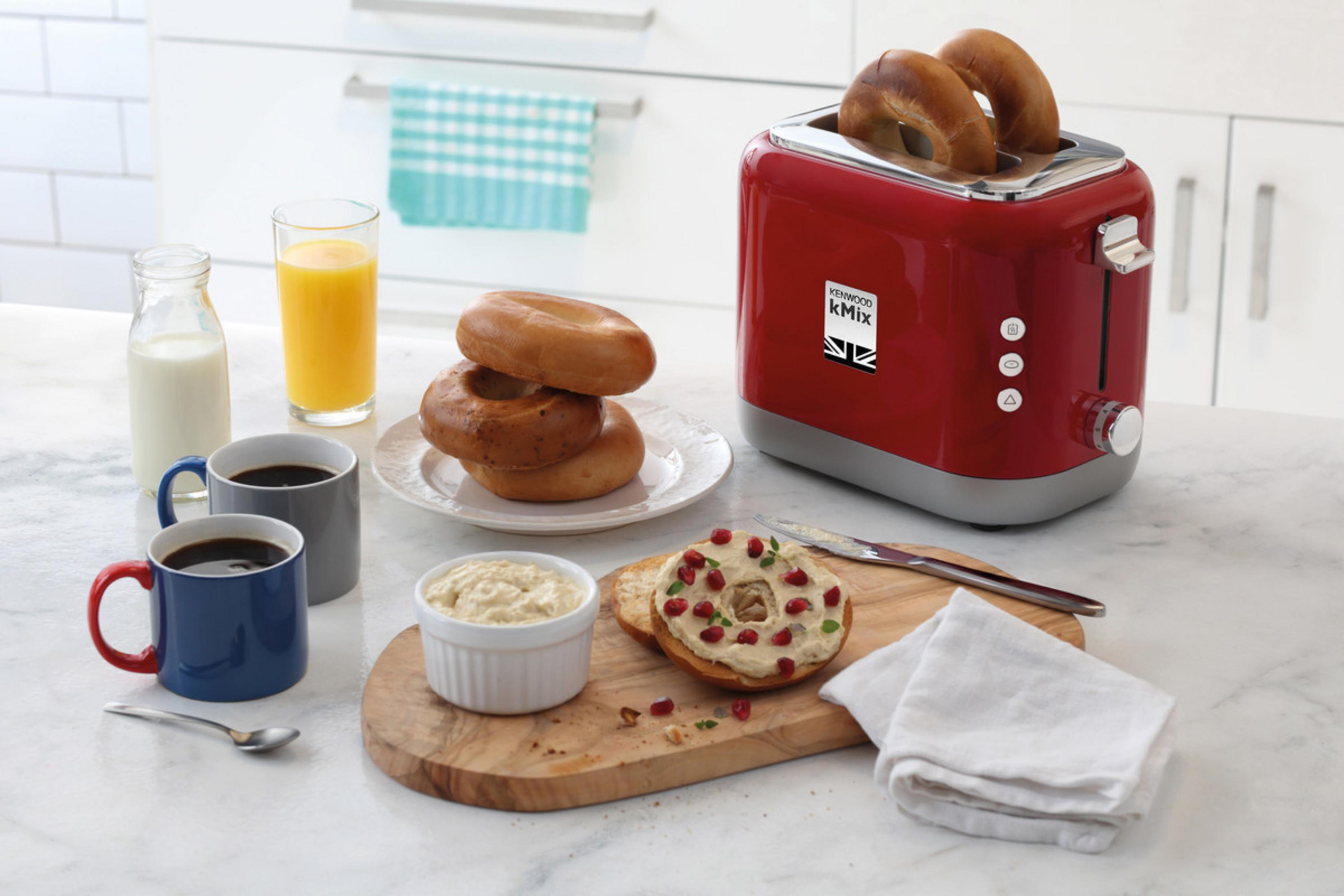 Scena della colazione: tostapane rosso con bagel, succo, caffè, formaggio cremoso e bagel a fette.