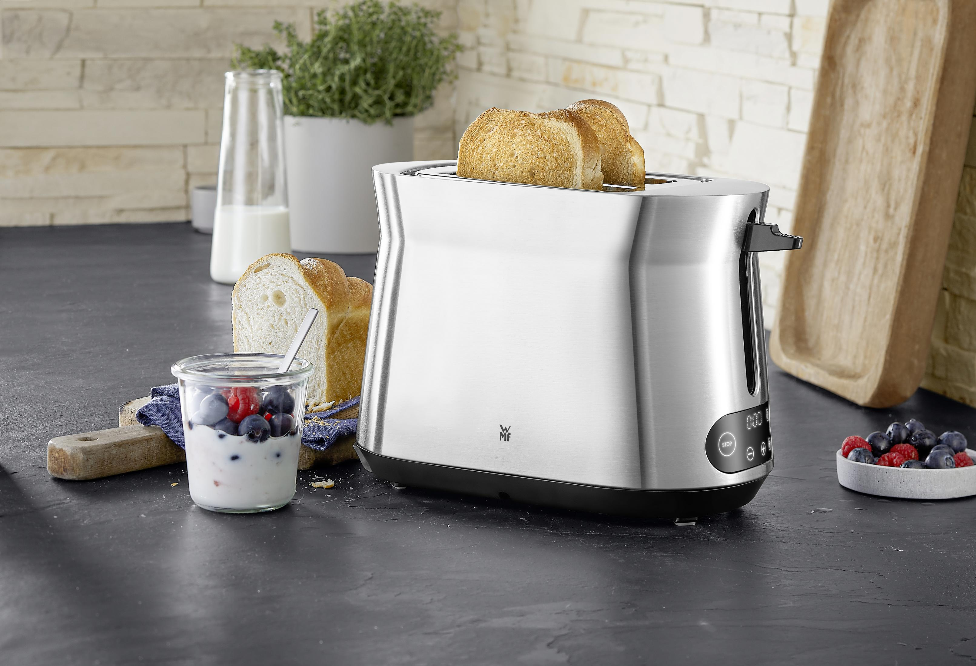 Toster ze stali nierdzewnej z dwoma kromkami tostów. Inne jedzenie i mleko są na blacie.