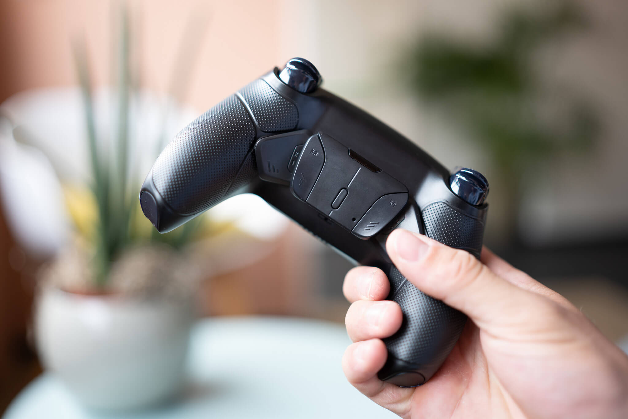Una mano che tiene un controller di gioco nero e grigio con impugnatura testurizzata e joystick blu.