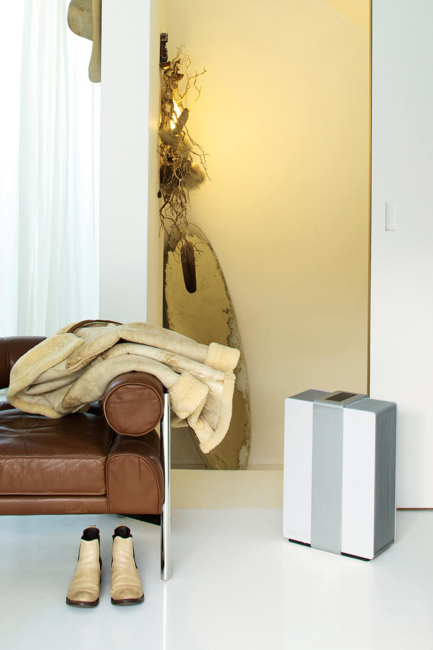 A room interior with a brown leather couch, boots, and a white air purifier next to a white door.