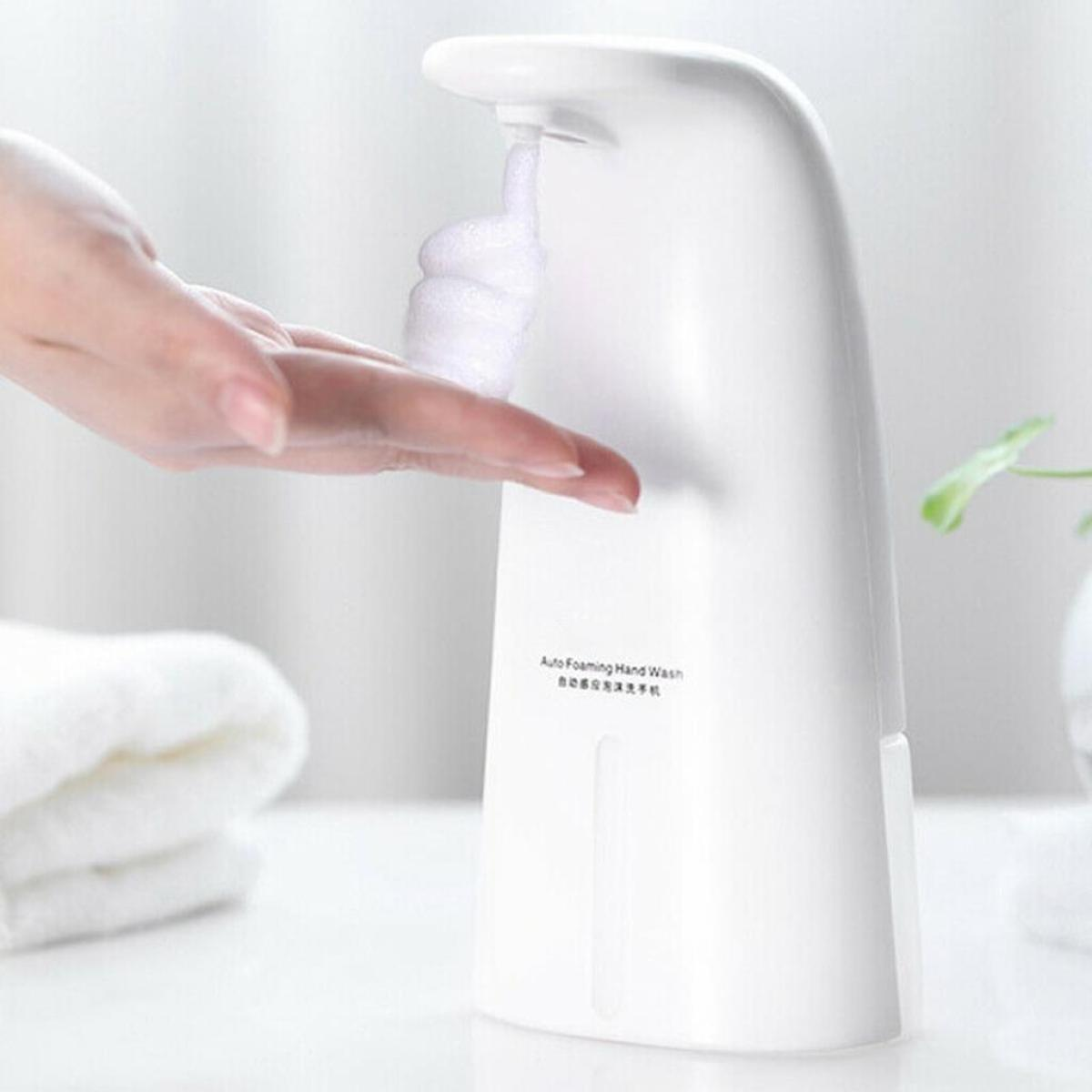 Weißer automatischer Schaumseifenspender. Hand greift nach Schaum. Weißer Hintergrund.