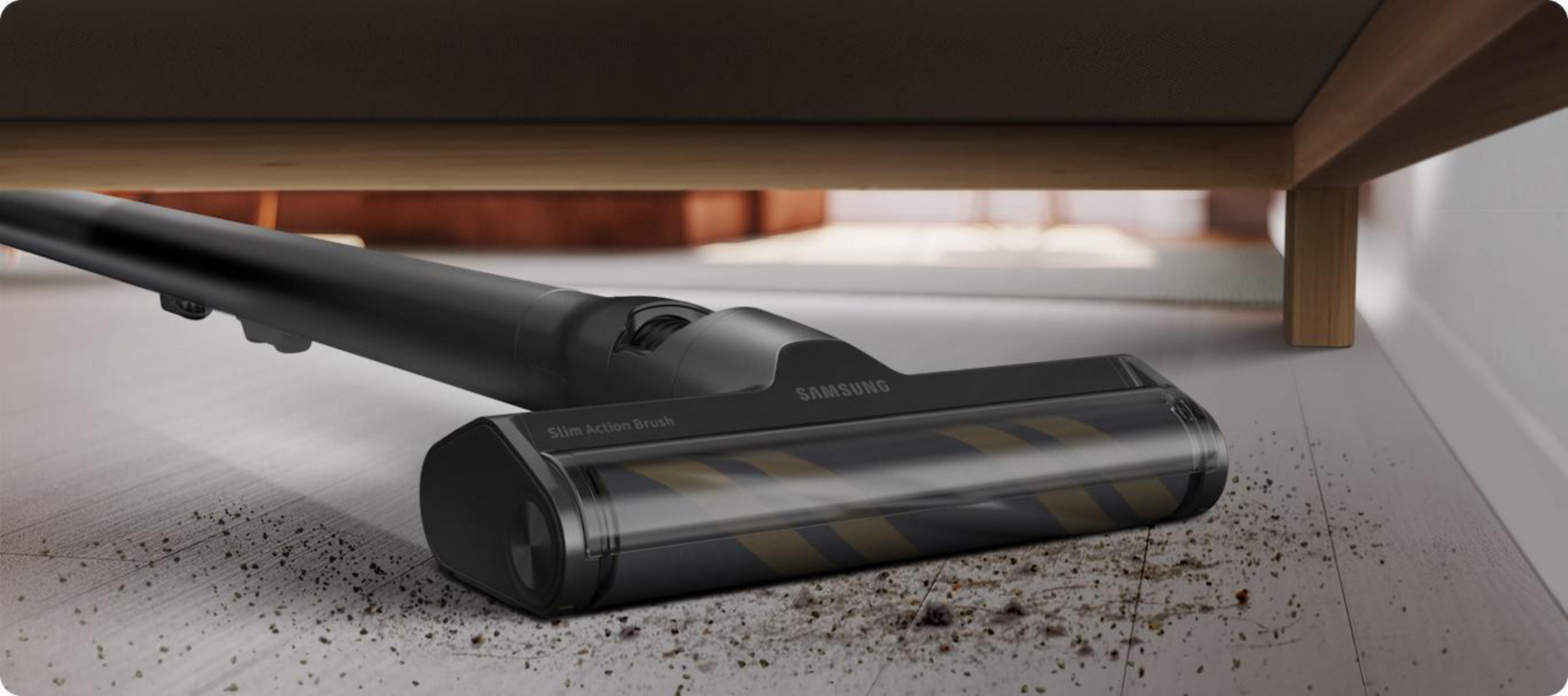Aspirapolvere Samsung nero sotto un mobile in legno, che pulisce un pavimento sporco. La testina è visibile.