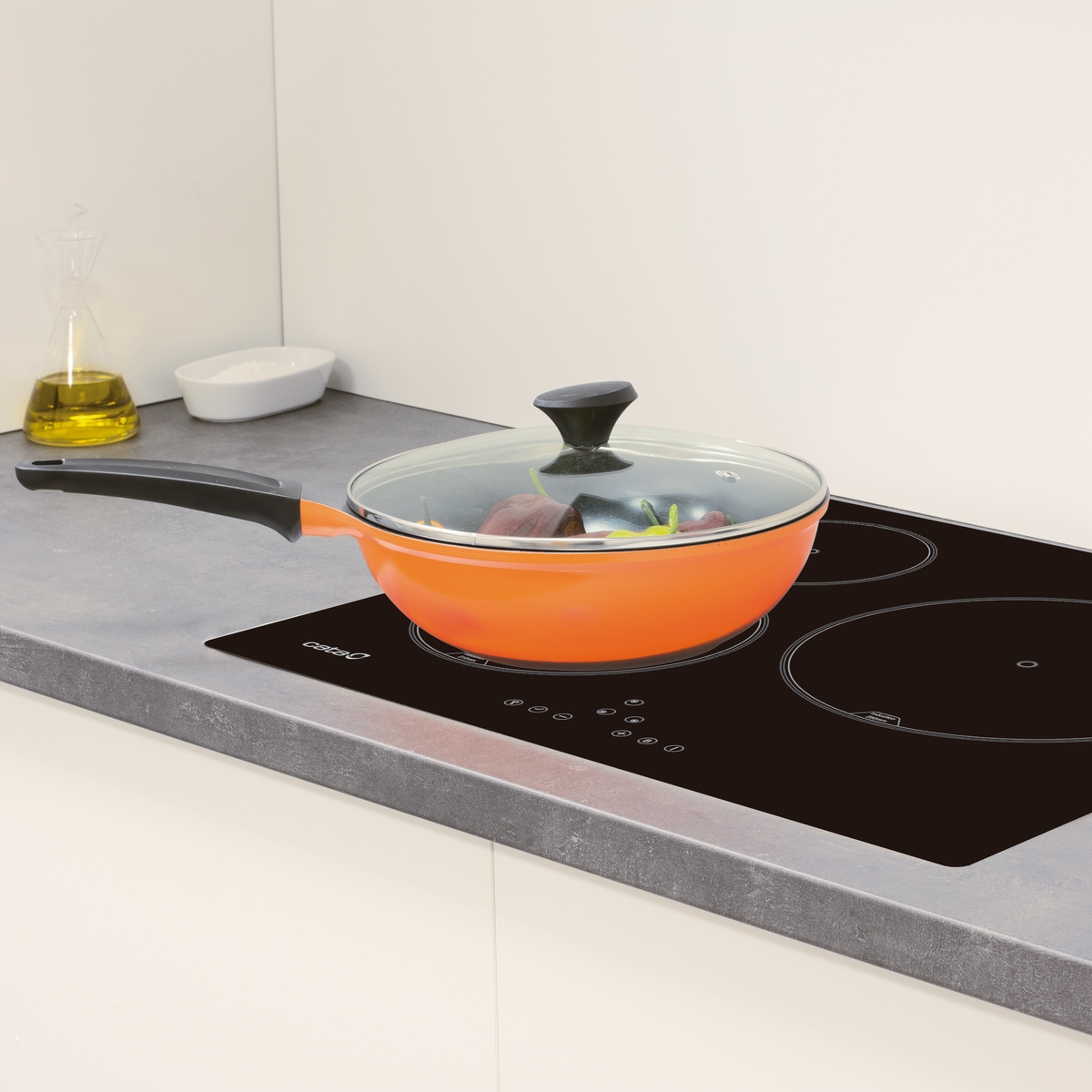 Sartén naranja con tapa de vidrio sobre una estufa negra. Fondo blanco. Mango negro.